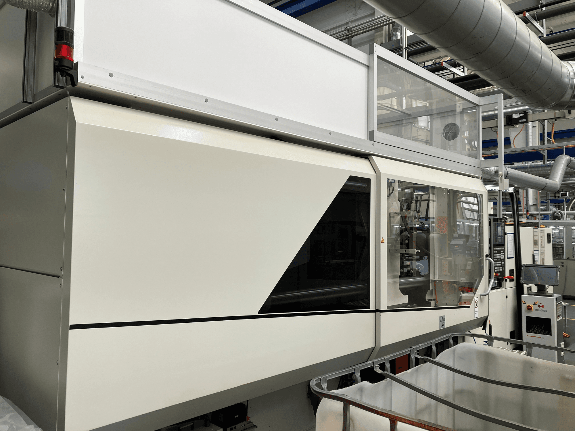 Ipari gép előlapja, elegáns fehér kialakítással, kijelzőpanellel és az alkatrészek láthatóságát biztosító üvegszekcióval.