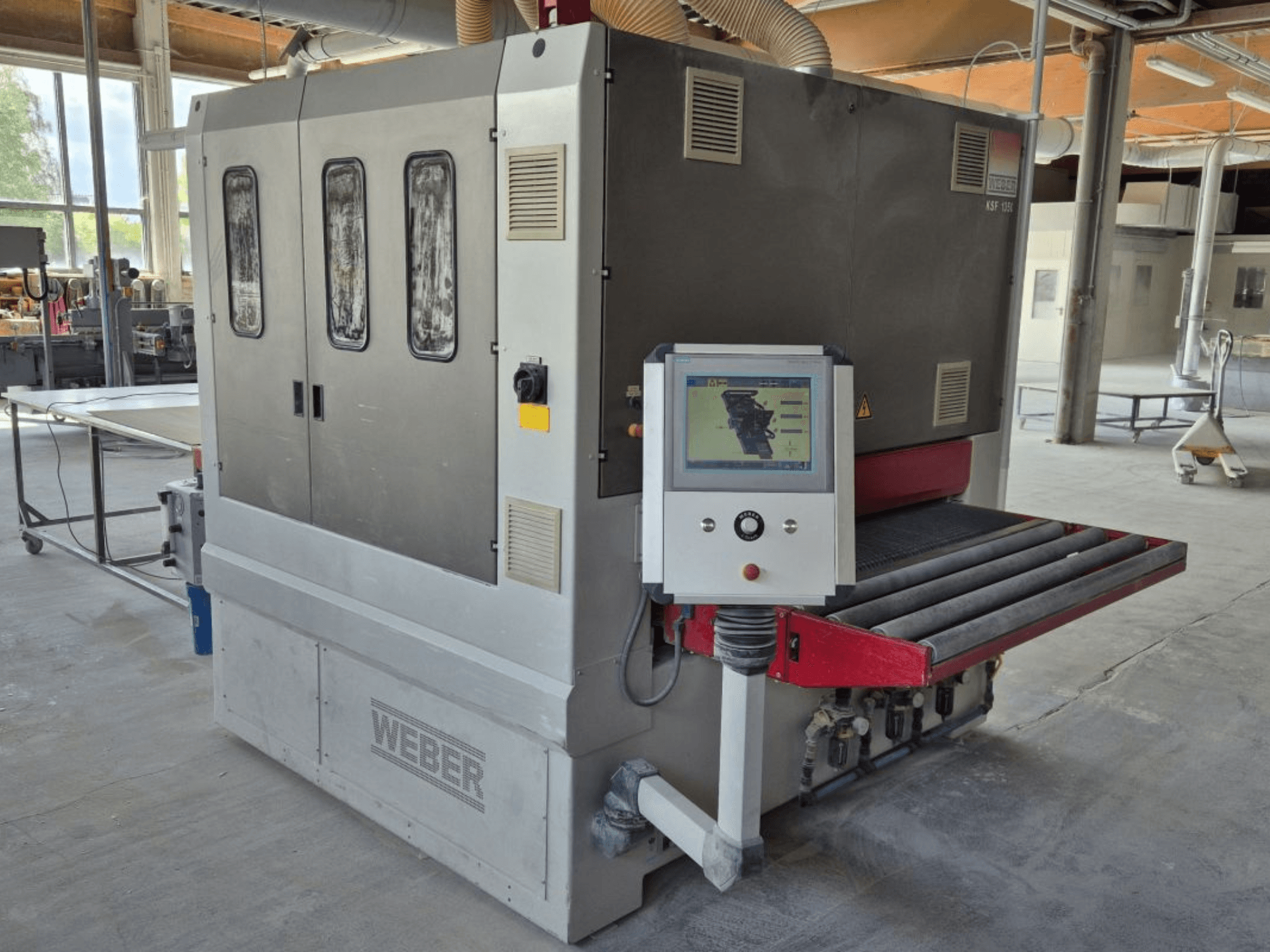 WEBER KSF-3-1350 szalagcsiszológép, oldalnézet a kezelőszervekkel, a teljesítménypanellel és a csiszolószalaggal. Ipari beállítás, látható gépekkel.