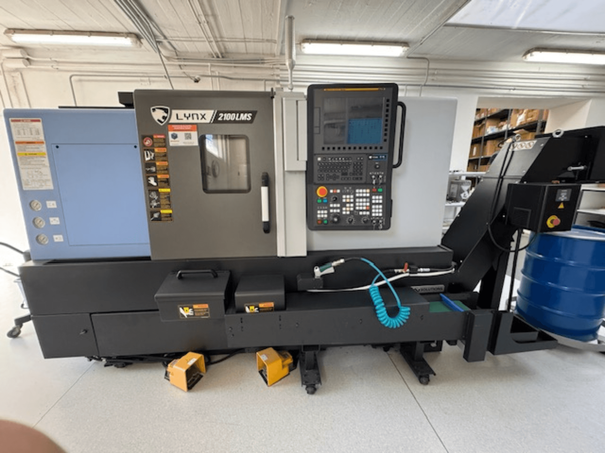 DOOSAN LYNX 2100LMSA vízszintes esztergagép, elölnézet, vezérlőpanel, hűtőfolyadék-tömlő és tárolódobozok.