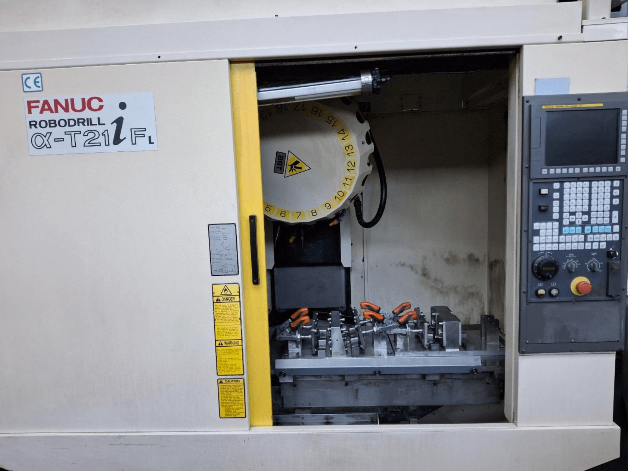 FANUC ROBODRILL α-T21iFL függőleges megmunkálóközpont előlnézetben, a szerszámok és a kezelőszervek a gépházban.