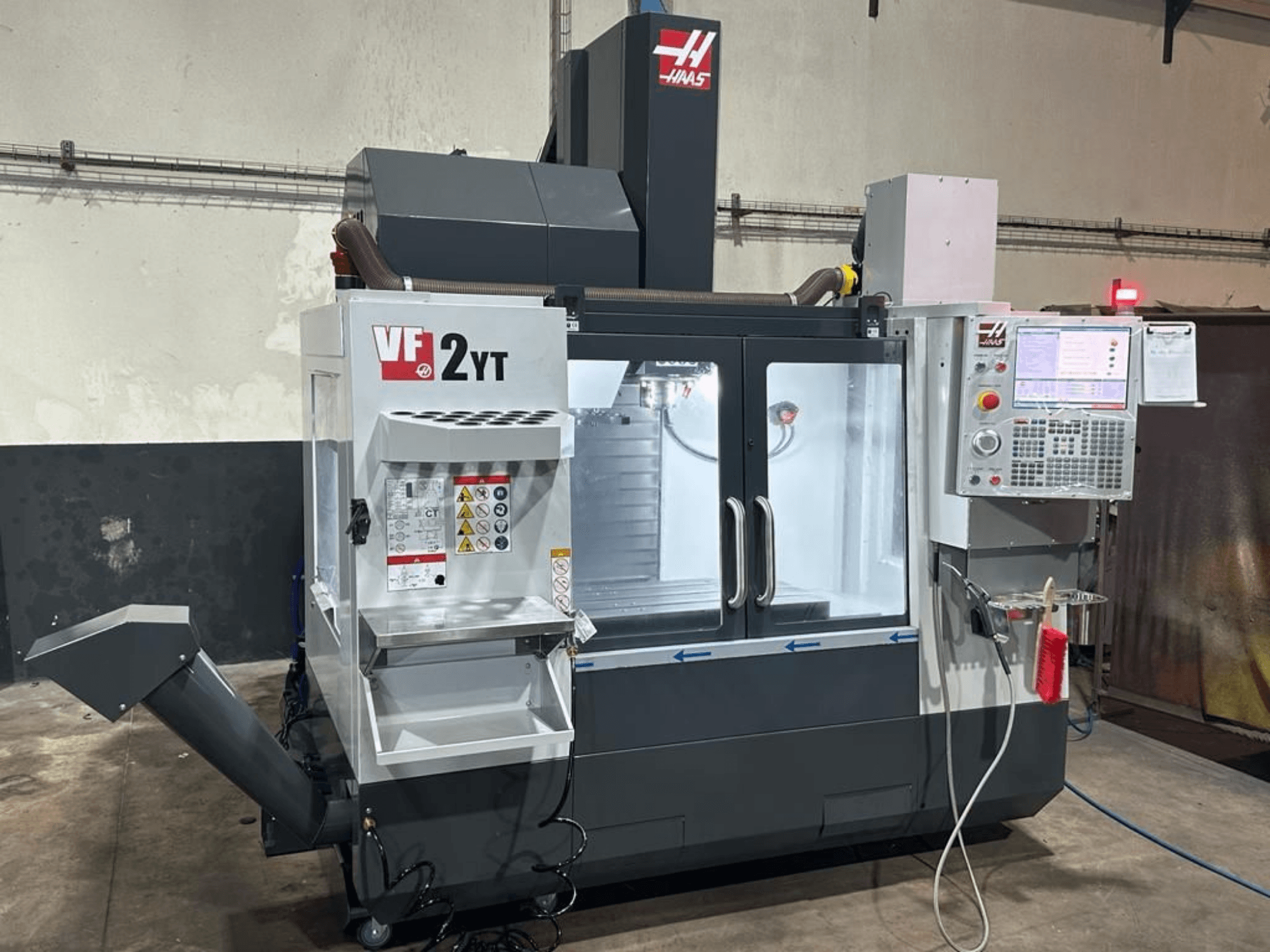 A HAAS VF-2YT-EU függőleges megmunkáló központ elölnézete, amelyen látható a vezérlőpanel és a szerszámtároló rekesz.