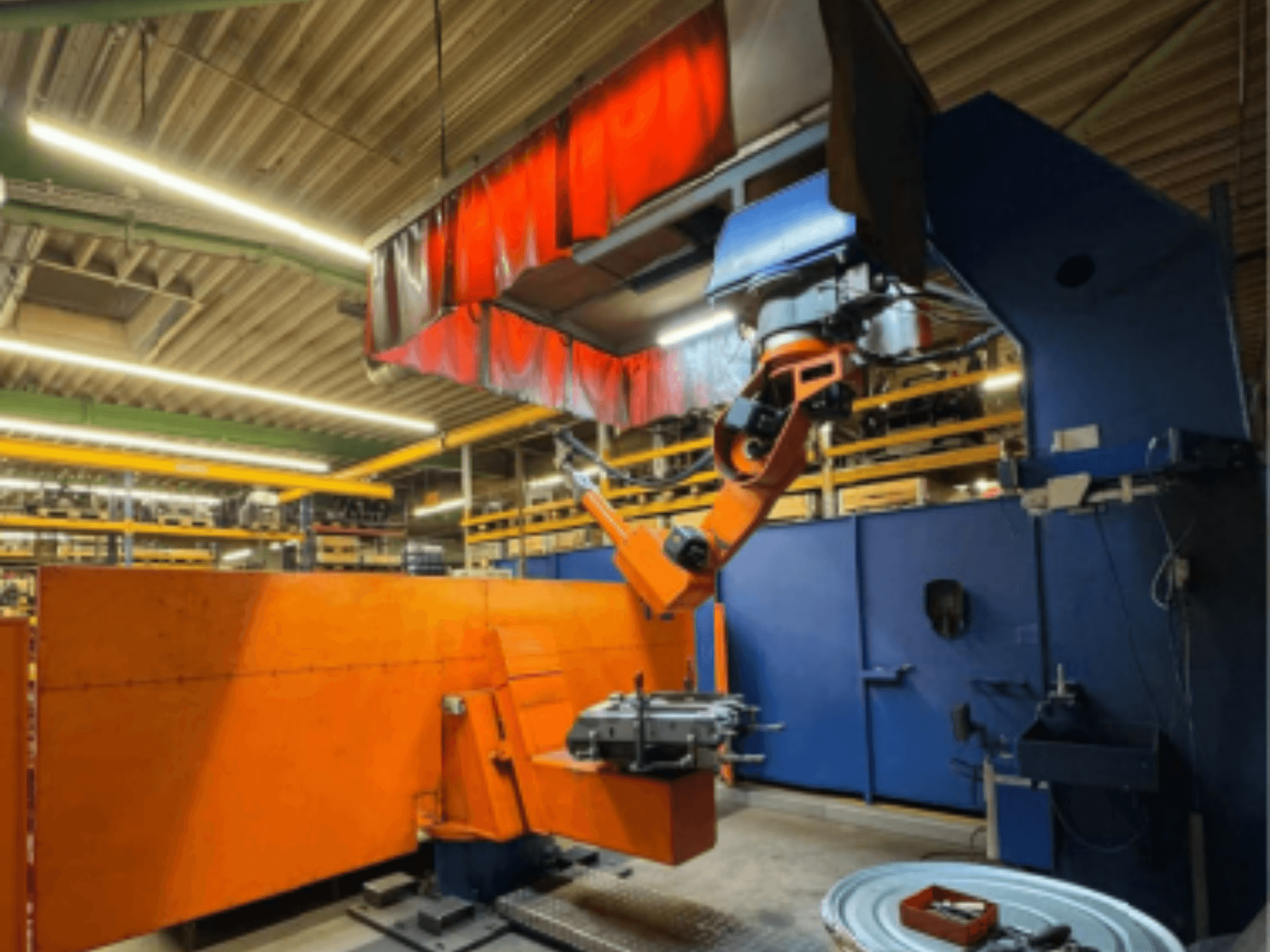 CLOOS Romat 350 e hegesztőrobot ipari környezetben, elölnézetben, narancssárga karral, munkadarabot tart a függöny alatt.