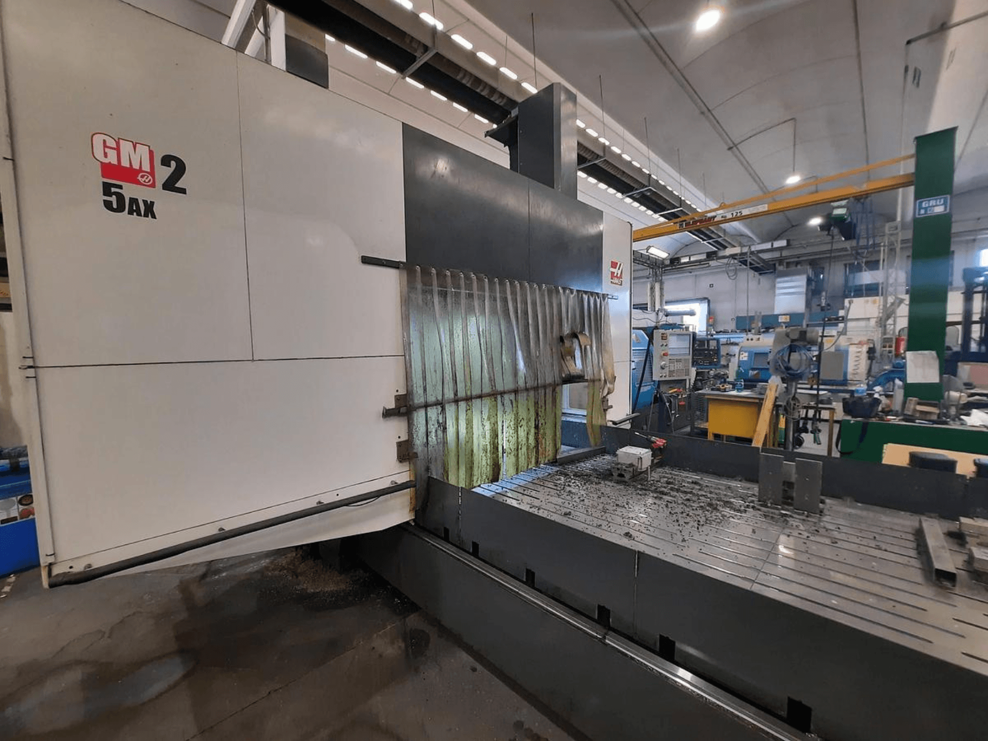 GM 2 5AX CNC-gép egy műhelyben, oldalnézet, a munkaterület és a fémforgácsok az ágy felületén.