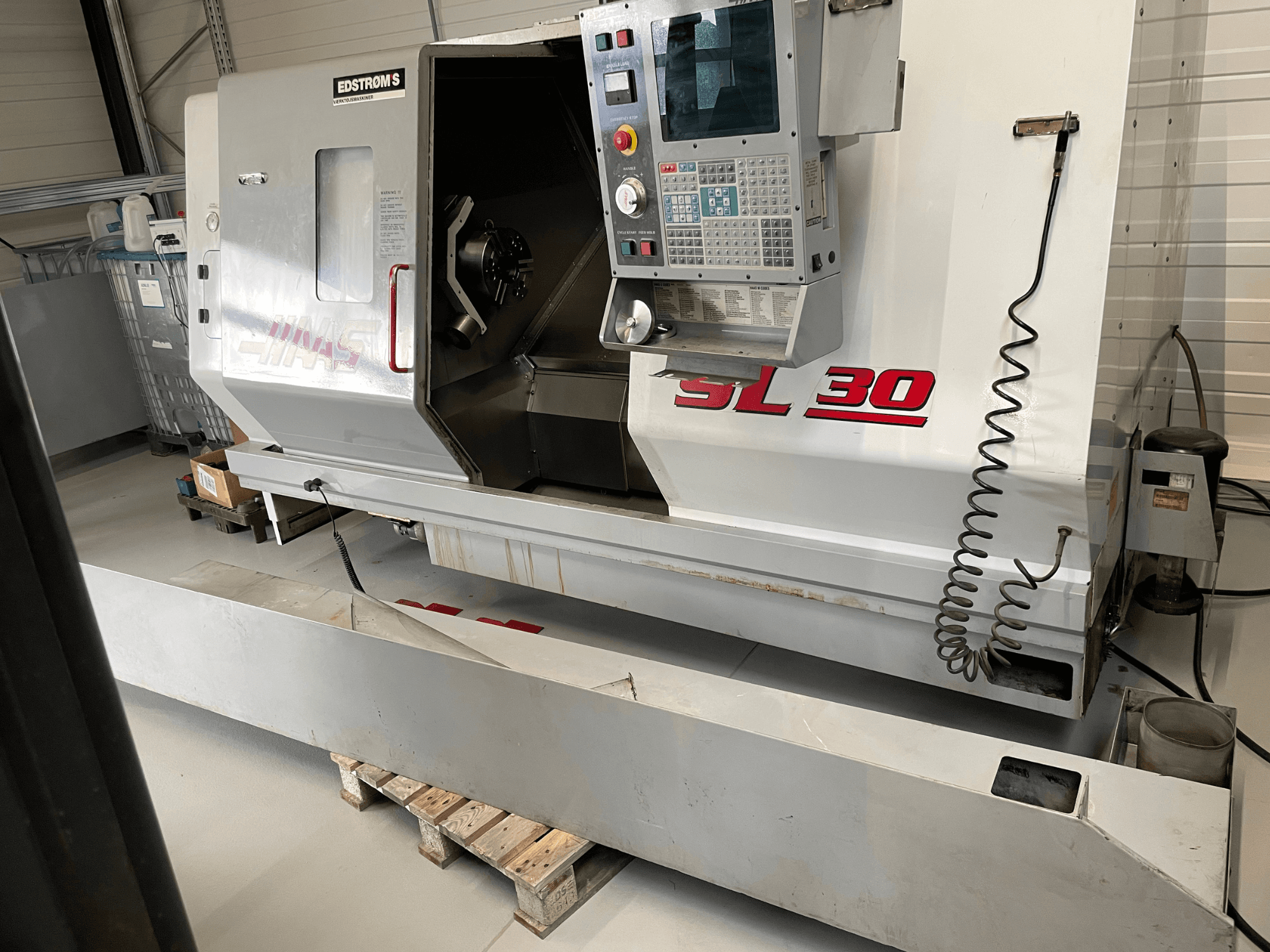 Haas SL 30 CNC esztergagép egy műhelyben, oldalnézet, vezérlőpanel és nyitott orsó a megmunkálási feladatokhoz.