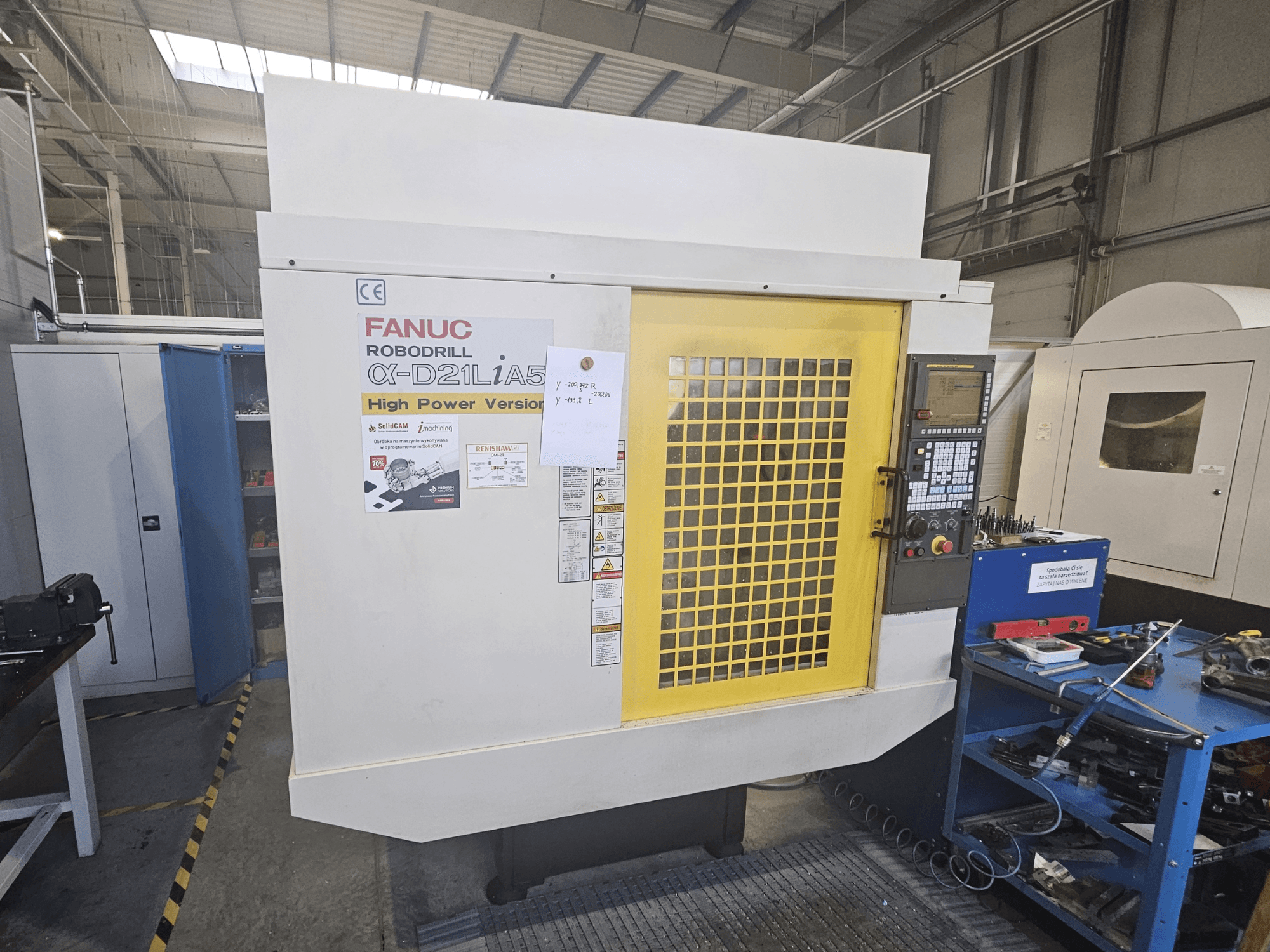 Egy FANUC Robodrill α-D21LiA5 előlapja sárga biztonsági ajtóval, vezérlőpanellel és a közelben lévő munkaterületi szerszámokkal.