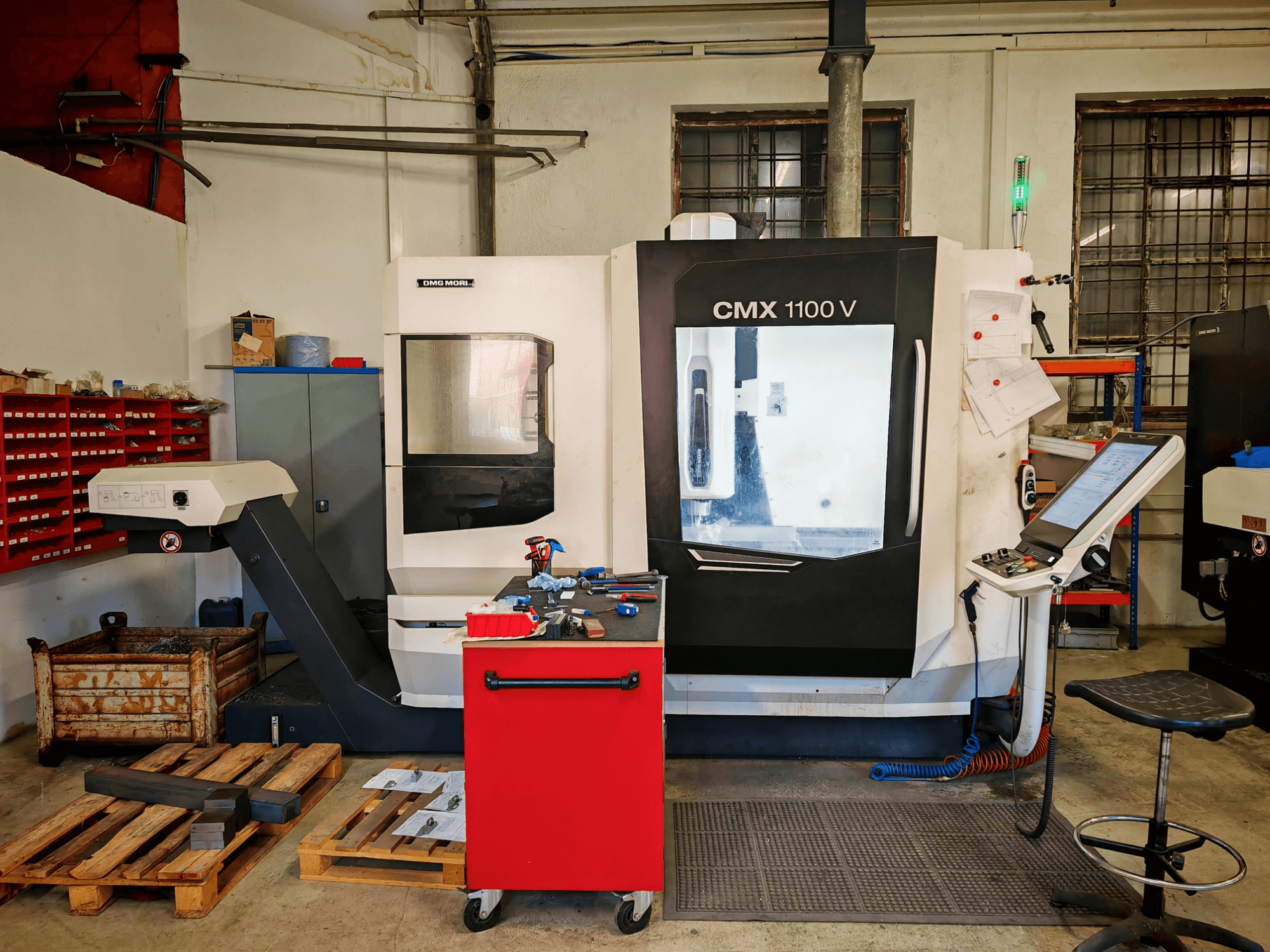 DMG MORI CMX 1100 V függőleges megmunkáló központ a műhelyben, elölnézetből, a vezérlőpanellel és a környező szerszámokkal.