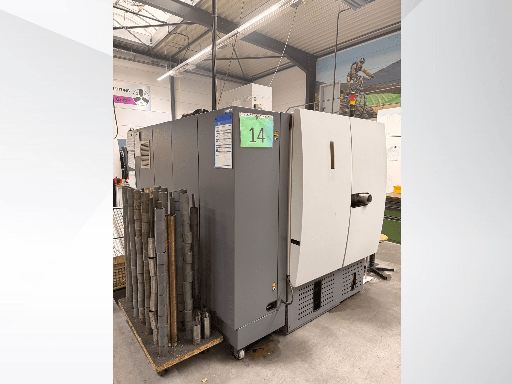 Szürke ipari gép a Siemens-től, oldalnézet, mellette hengeres fémdarabok készlete és láthatóak a berendezések címkéi.