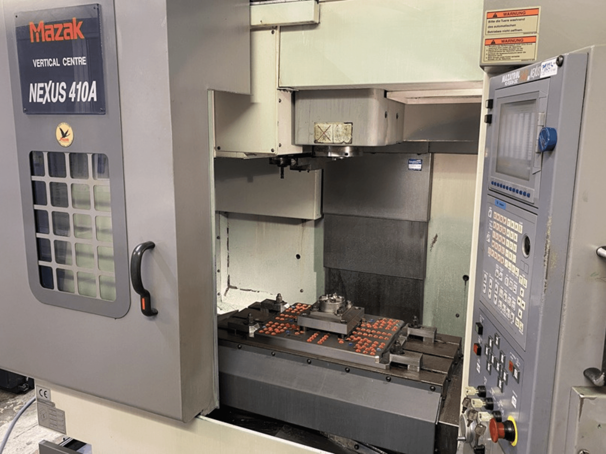 Mazak VCN410 függőleges megmunkálóközpont, elölnézetben a vezérlőpanel és a gép belseje a munkadarab felszerelésével.