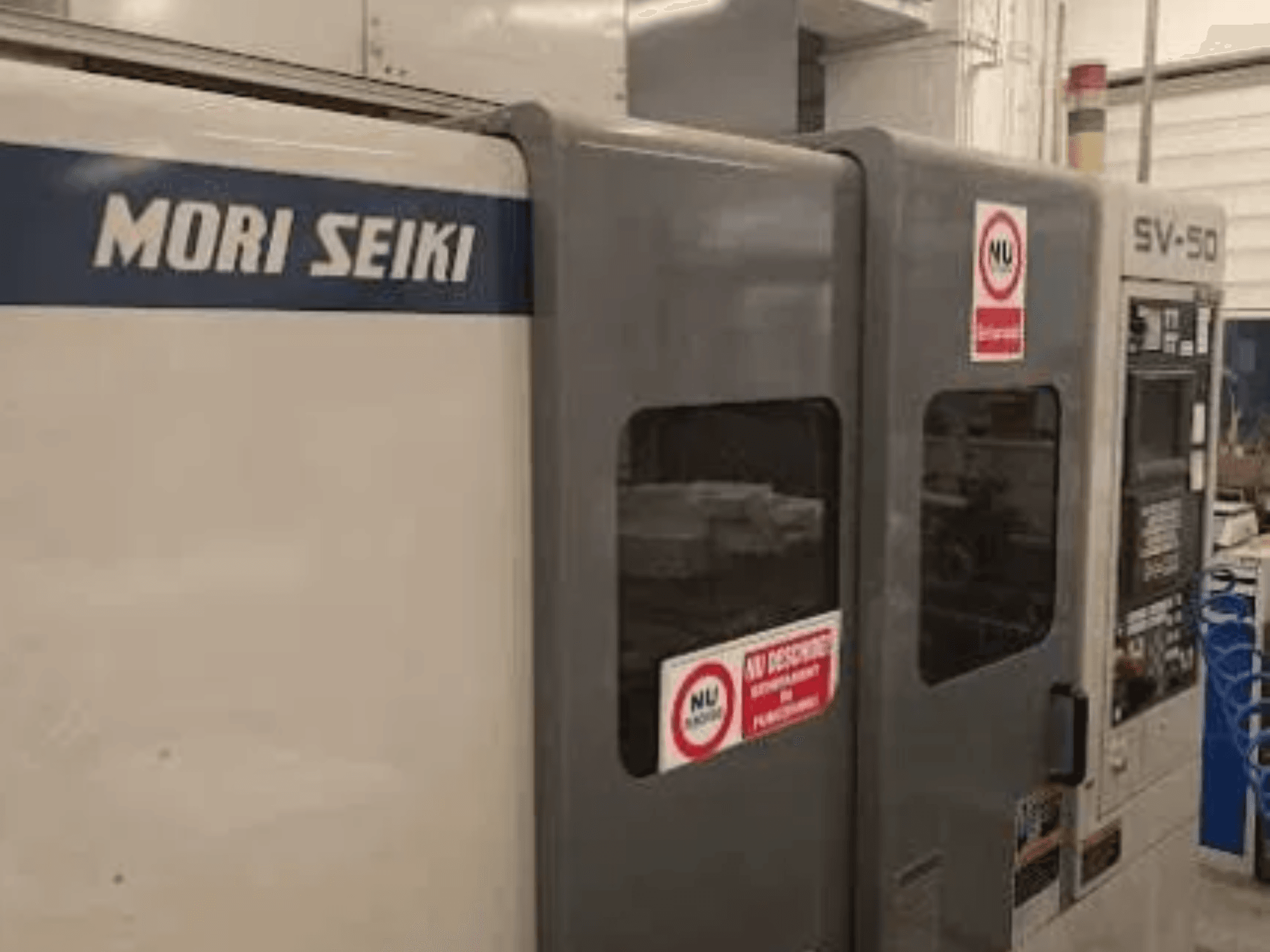 MORI SEIKI SV-50 CNC gép, oldalnézet; vezérlőpanel és biztonsági figyelmeztető matricák.