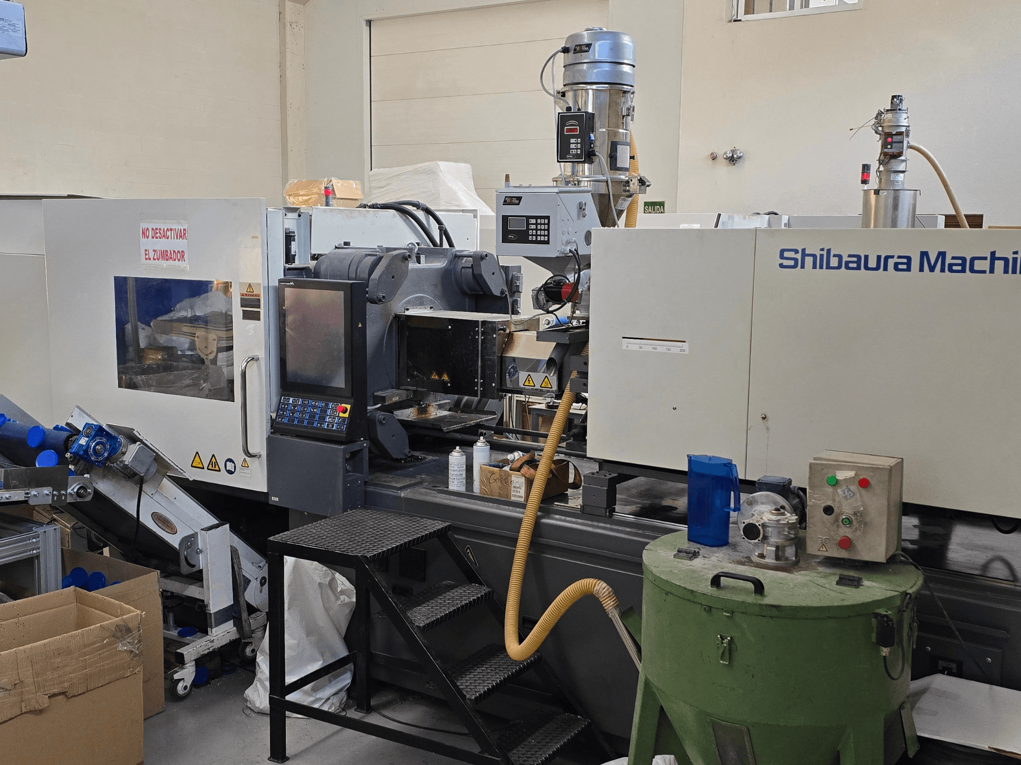A SHIBAURA EC230SXIII-8A elektromos fröccsöntőgép elülső nézete a vezérlőpanellel és a szomszédos berendezésekkel.