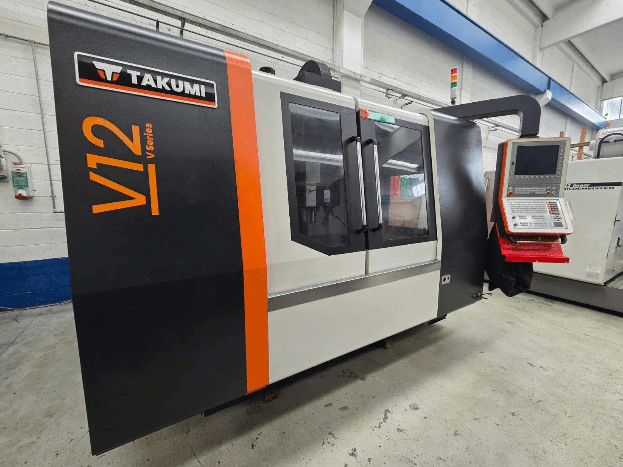 Takumi V12 V sorozatú CNC marógép, előlnézet, vezérlőpanel és nagy üvegablakok.