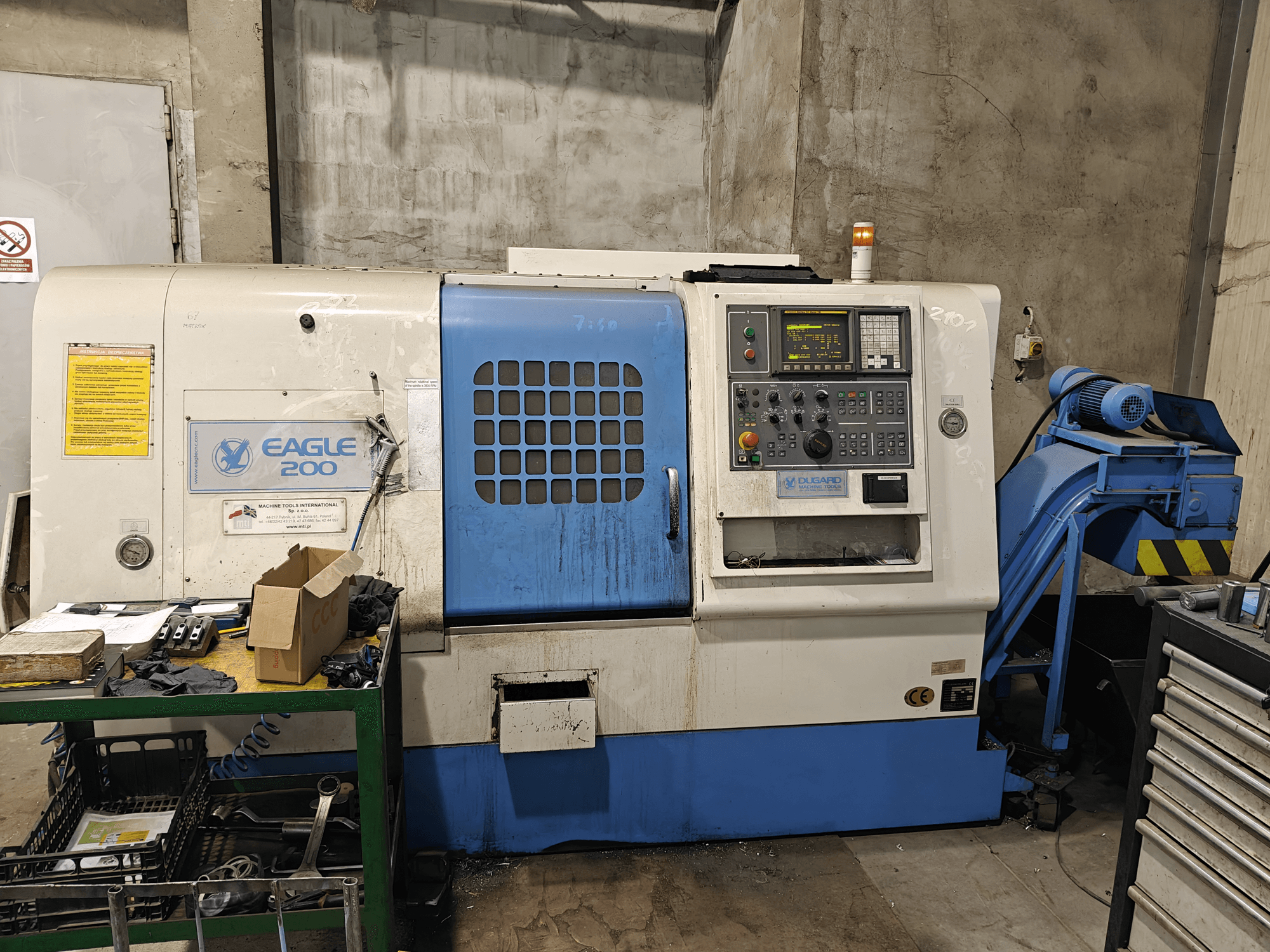 Eagle 200 CNC-gép, elölnézet a vezérlőpanellel, különböző szerszámok egy zöld kocsin. Látható kopás és működési lámpák.