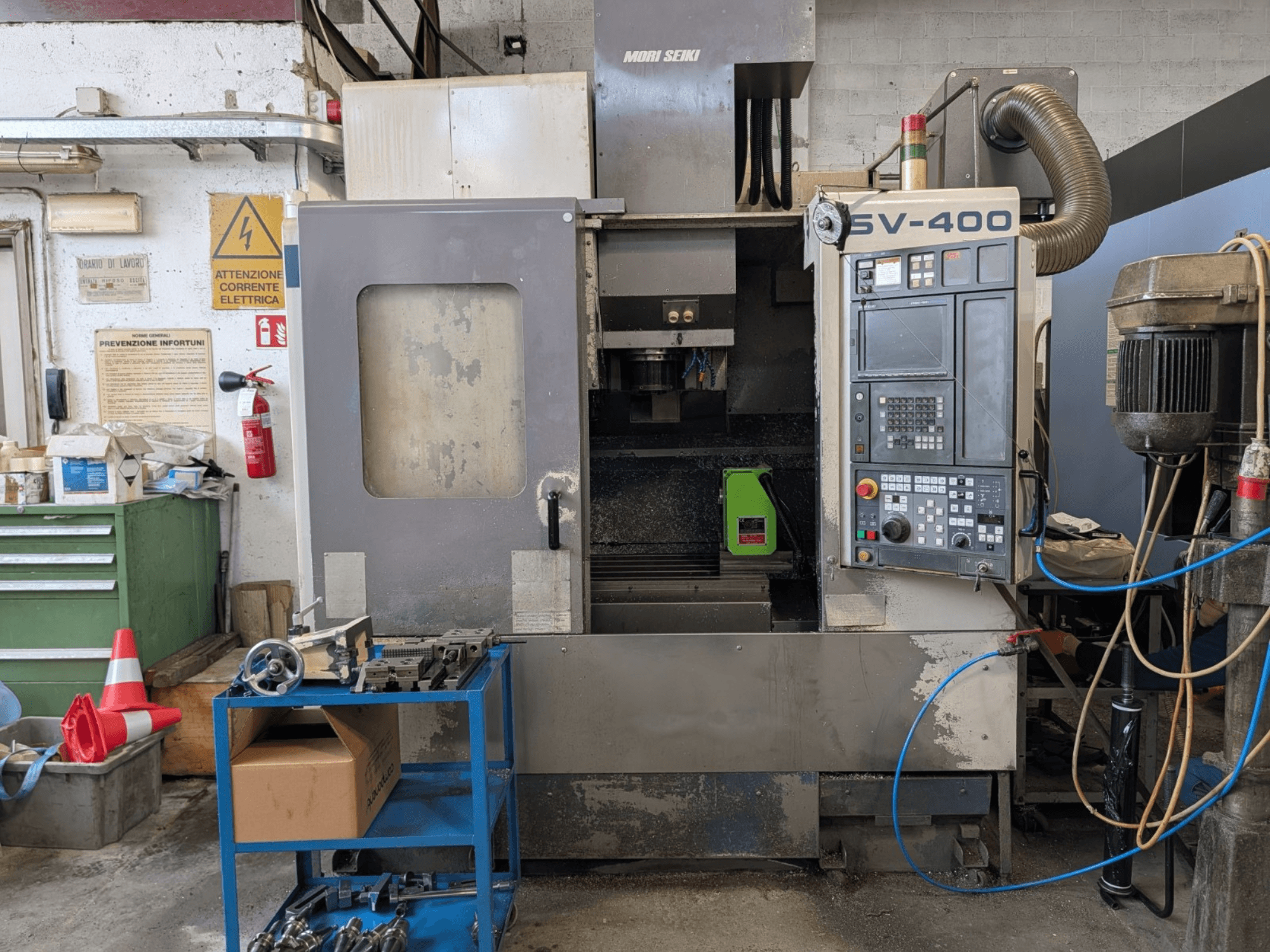 MORI SEIKI SV-400 függőleges megmunkálóközpont egy műhelyben, oldalnézet, a vezérlőpanel és a szerszámgépek a közelben.