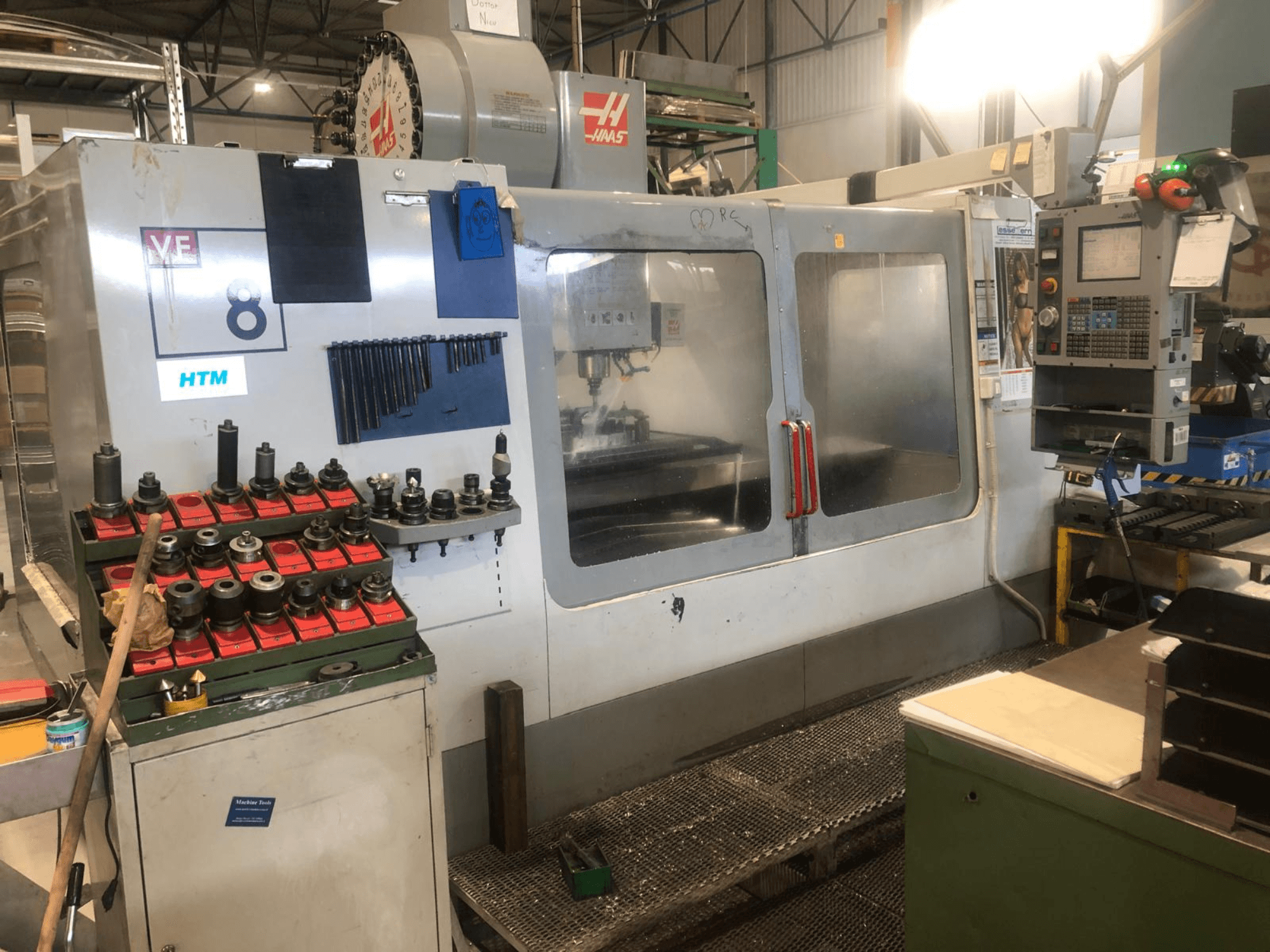 Haas CNC-gép egy műhelyben, elölnézetben; szerszámok és kezelőszervek, látható modellrészletekkel és rendezett szerszámtartókkal.