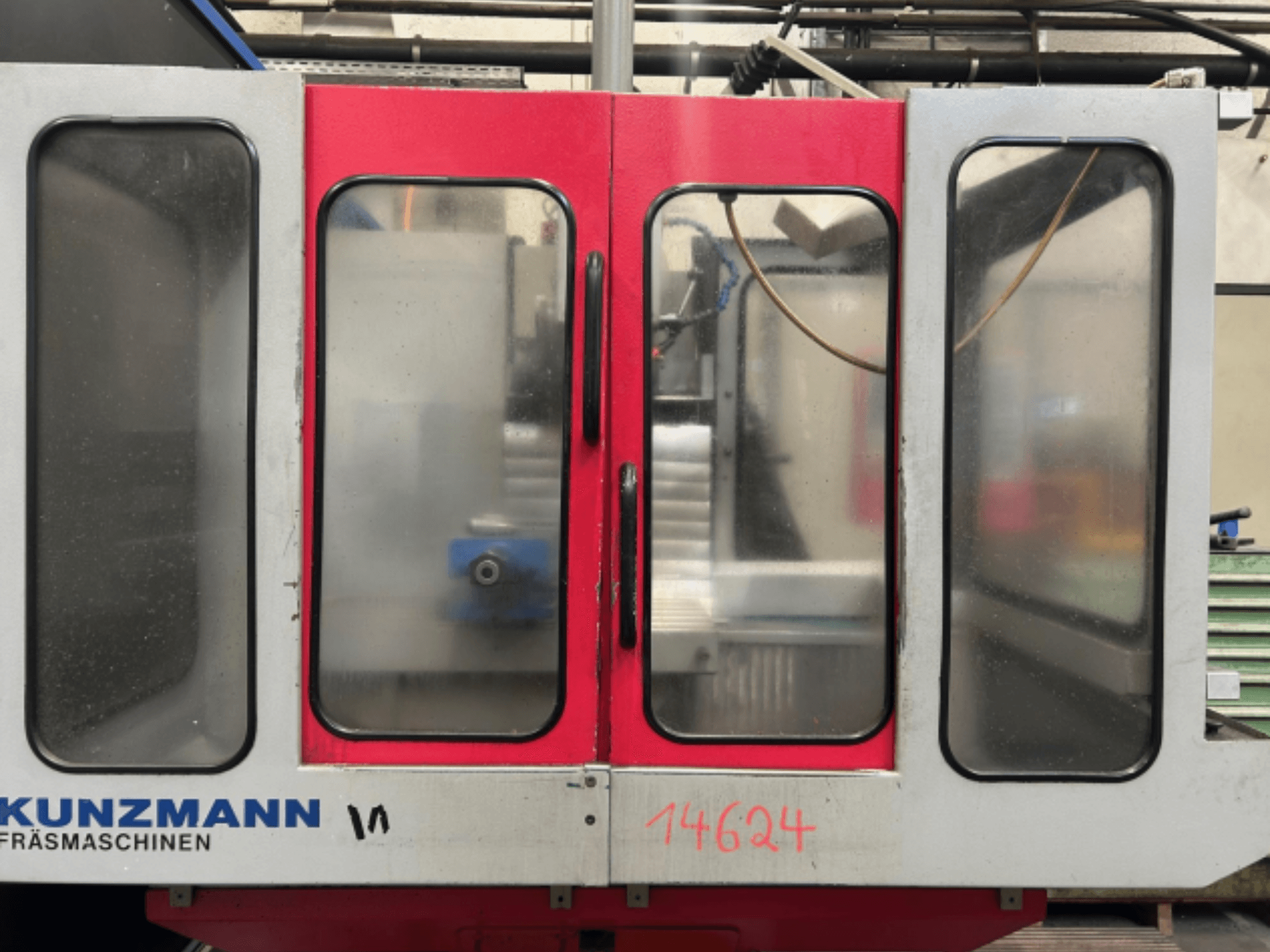 KUNZMANN CNC-gép előlapja, piros és szürke panelekkel, belül látható vezérlőpanel és szerszámtartó.