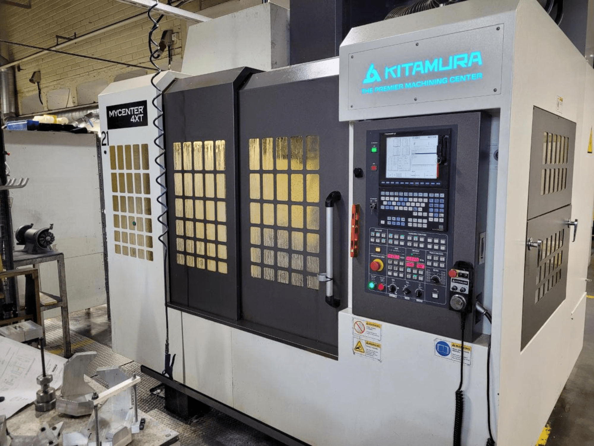 Egy Kitamura Mycenter-4XT megmunkálóközpont függőleges nézete, vezérlőpanellel és megvilágított márkajelzéssel.