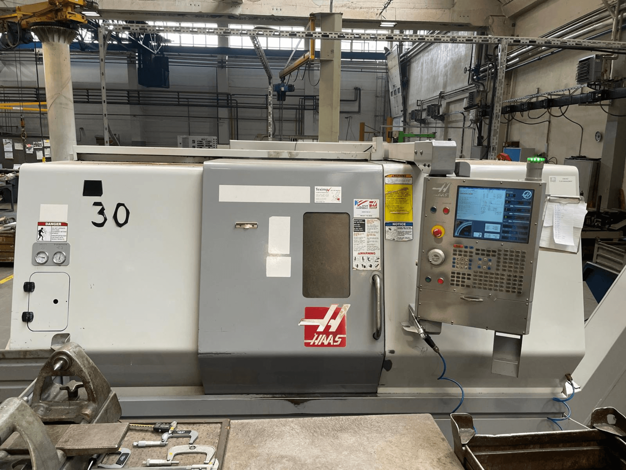 A Haas SL-30THE vízszintes eszterga elölnézete, digitális vezérlőpanellel, figyelmeztető címkékkel és a 30-as típusszámmal.