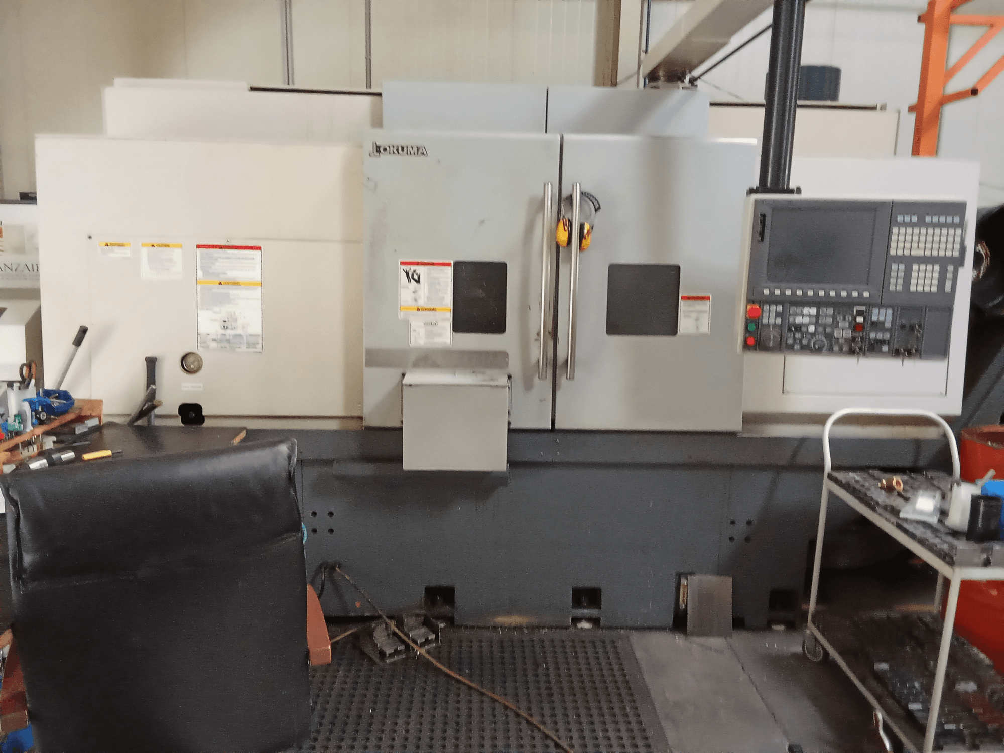 Okuma Genos L300 E-M vízszintes esztergagép elölnézetben, a vezérlőpanel és a kettős ajtók bemutatásával, műhelykörnyezetben.