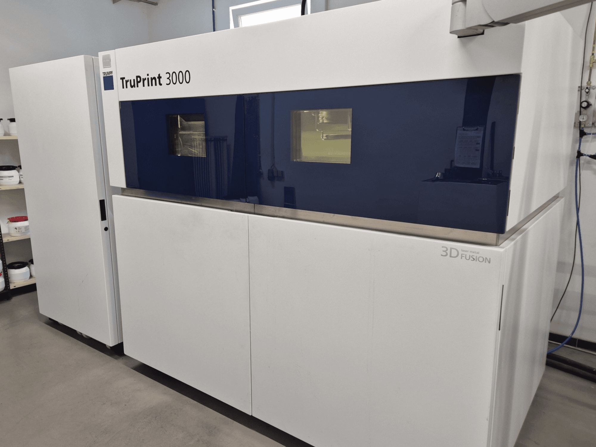 TruPrint 3000 fém 3D nyomtató elölnézetben, kék színű kialakítással és lézerfúziós technológiával.