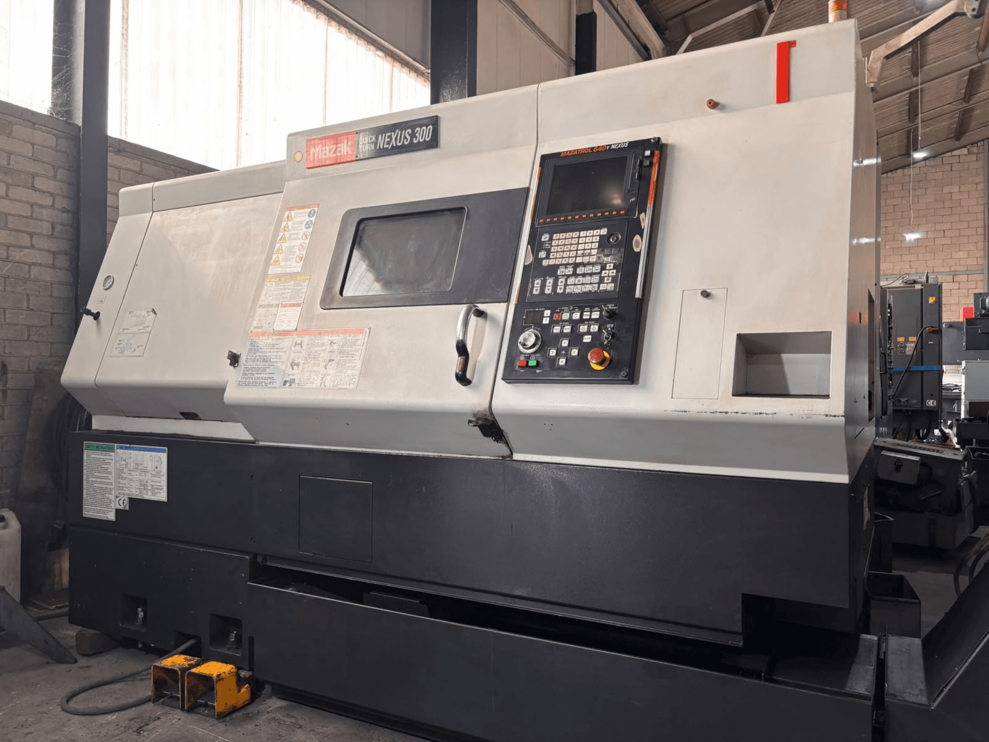Mazak QT NEXUS 300 vízszintes eszterga, oldalnézet a vezérlőpanelről és a működési jelzőfényekről egy műhelyi környezetben.