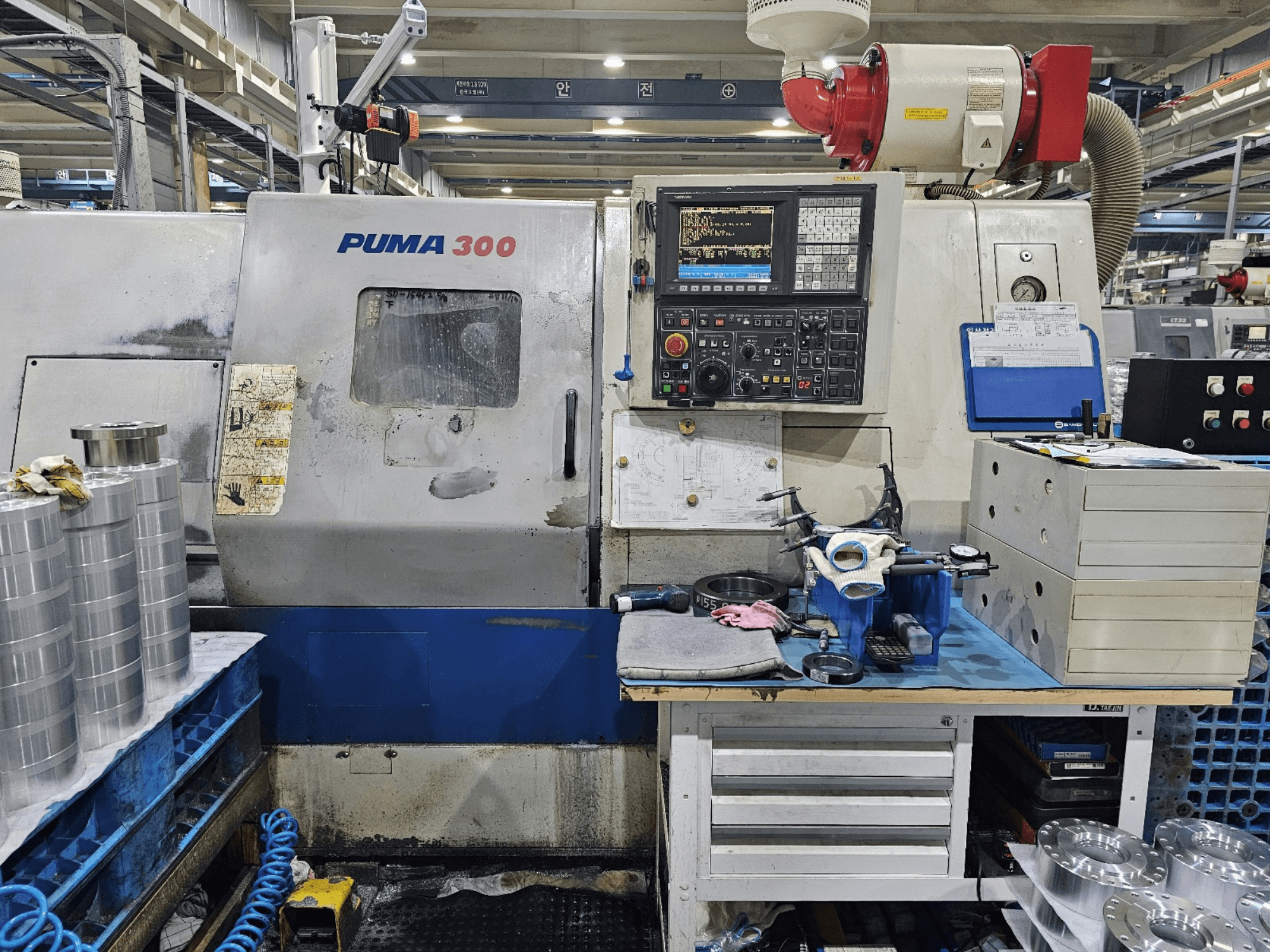 PUMA 300 CNC-gép egy műhelyben; elölnézetben a vezérlőpanel, a szerszámok és a fém alkatrészek a munkapadon.