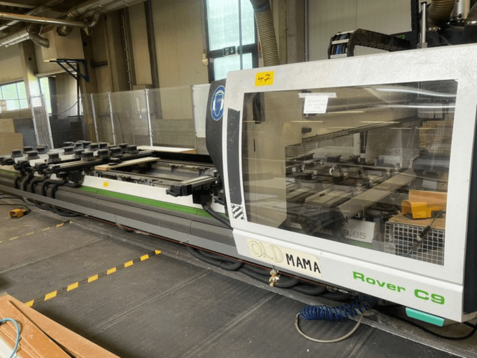 BIESSE Rover C 9.65 CNC marógép egy műhelyben, oldalnézetben a kezelőpanel és a munkaasztal rögzítőkkel.