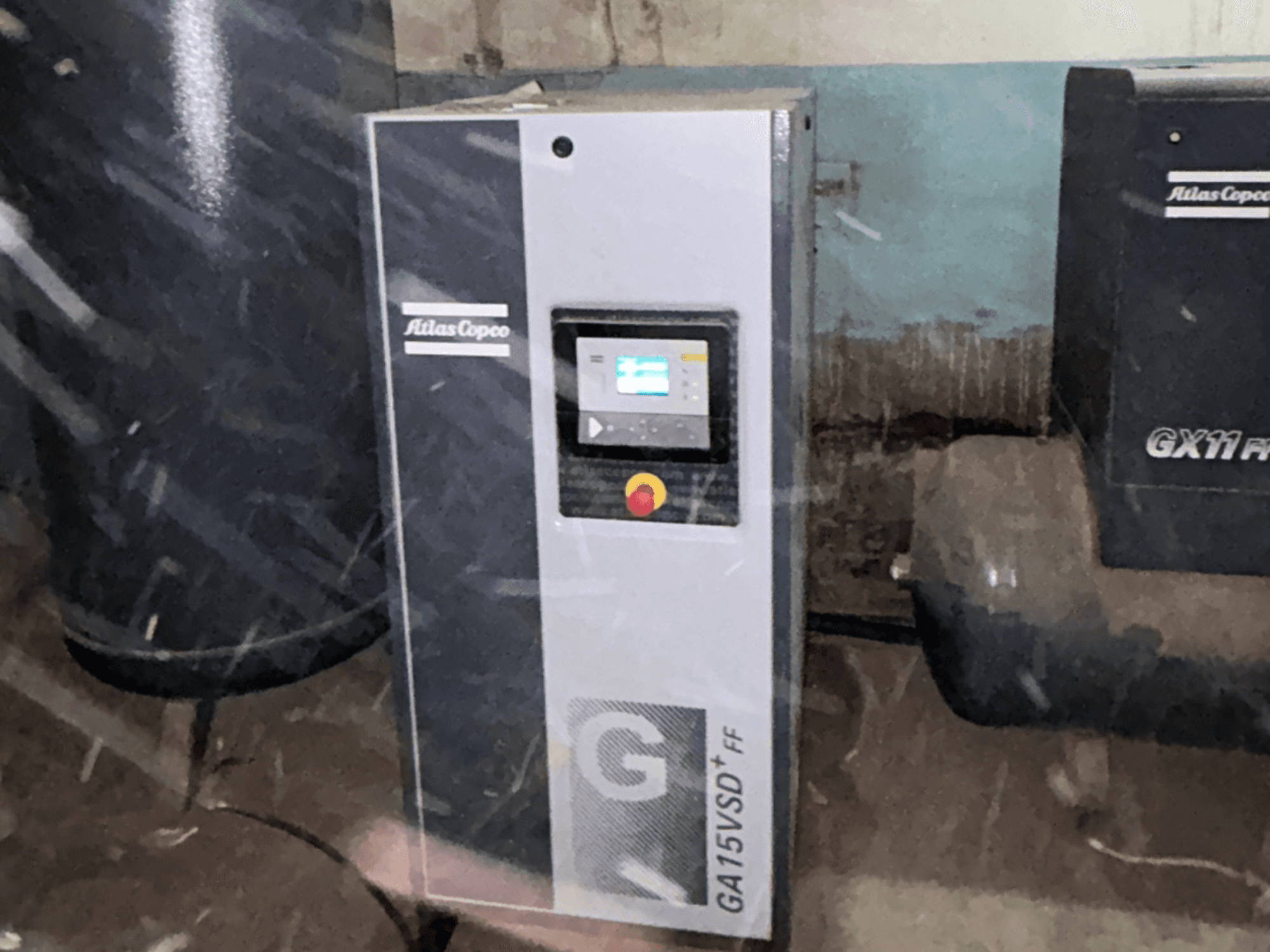 Atlas Copco GA15VSD+FF légkompresszor, elölnézet, kijelzős vezérlőpanellel és piros vészleállító gombbal.