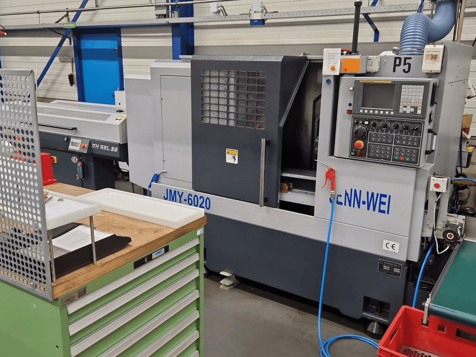 CNC esztergagép, a cNN-WEI JMY-6020 modellje, szemből nézve. Vezérlőpanel, vészleállító és hűtőfolyadék-vezeték.