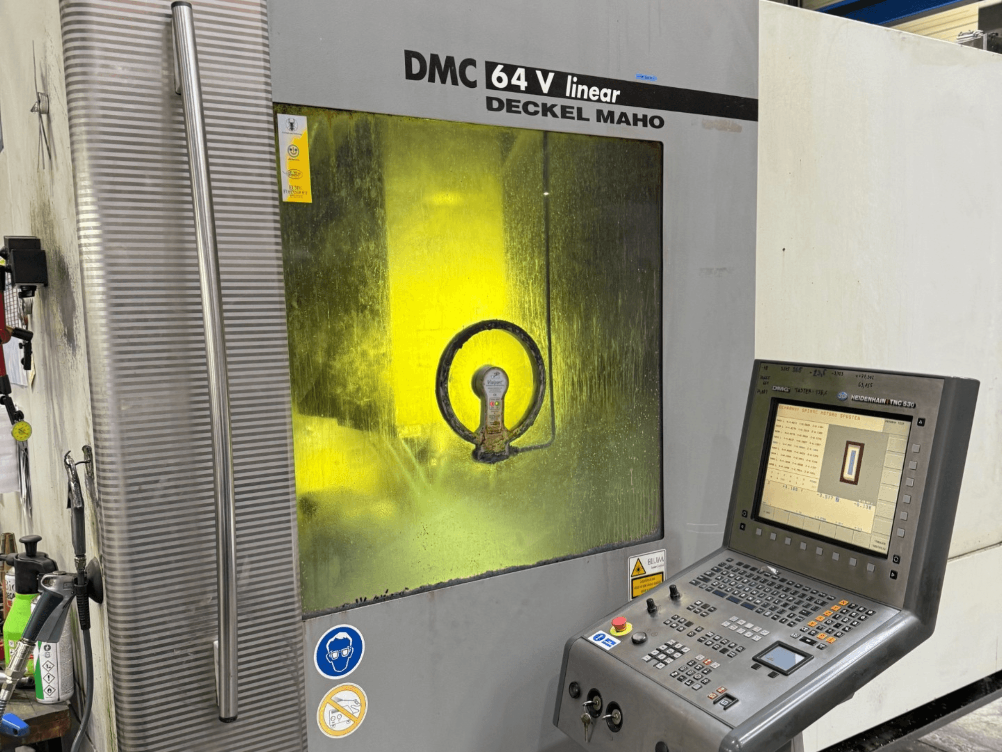 DMC 64 V lineáris, Deckel Maho, a gép előlapja, vezérlőpanel és sárga színű ablak, amely a belső mechanizmusokat mutatja.