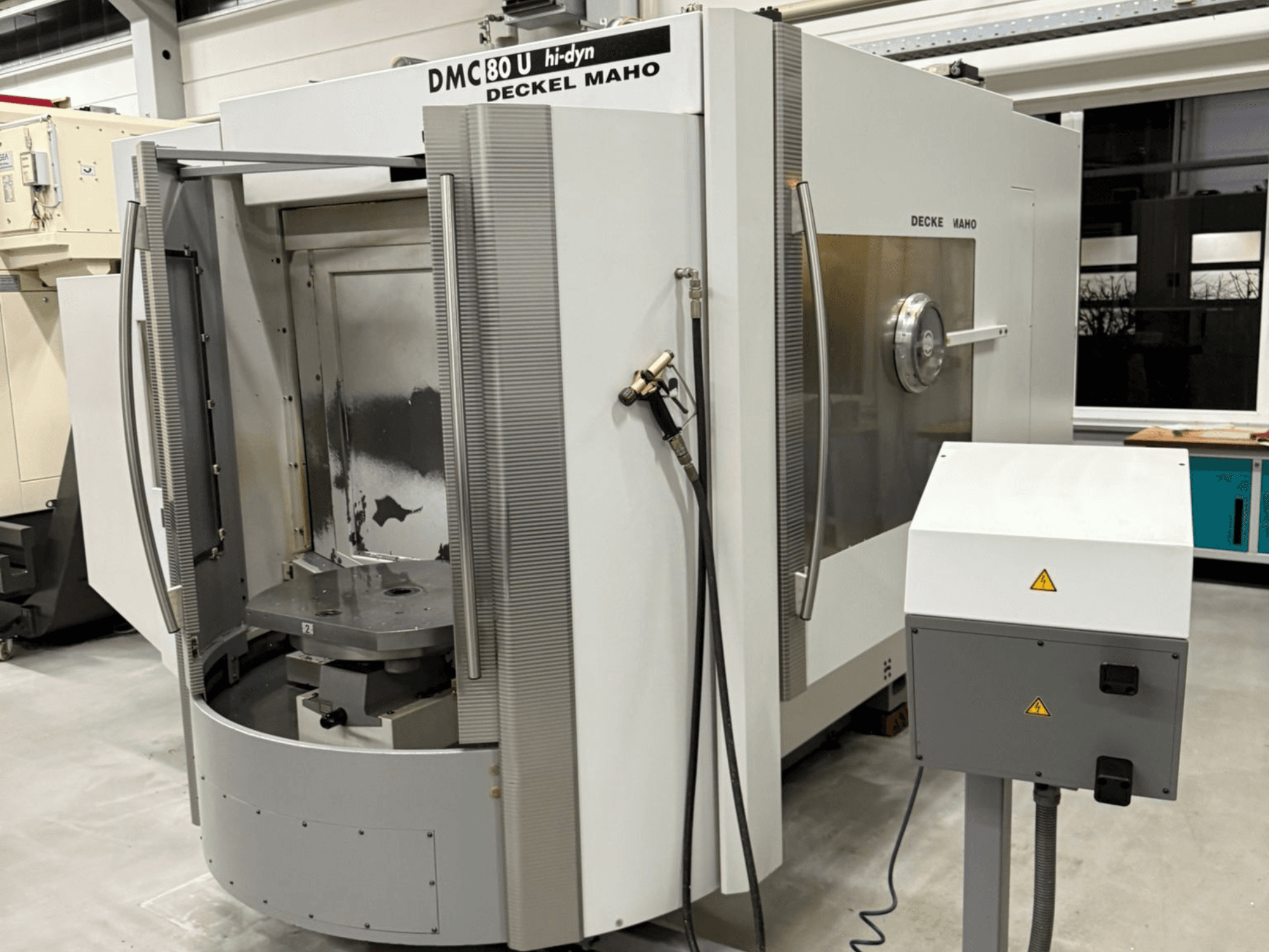 Egy Deckel Maho DMC 80 U nagysebességű CNC marógép előlapja, nyitott bejárati ajtóval és az oldalsó vezérlőpanellel.