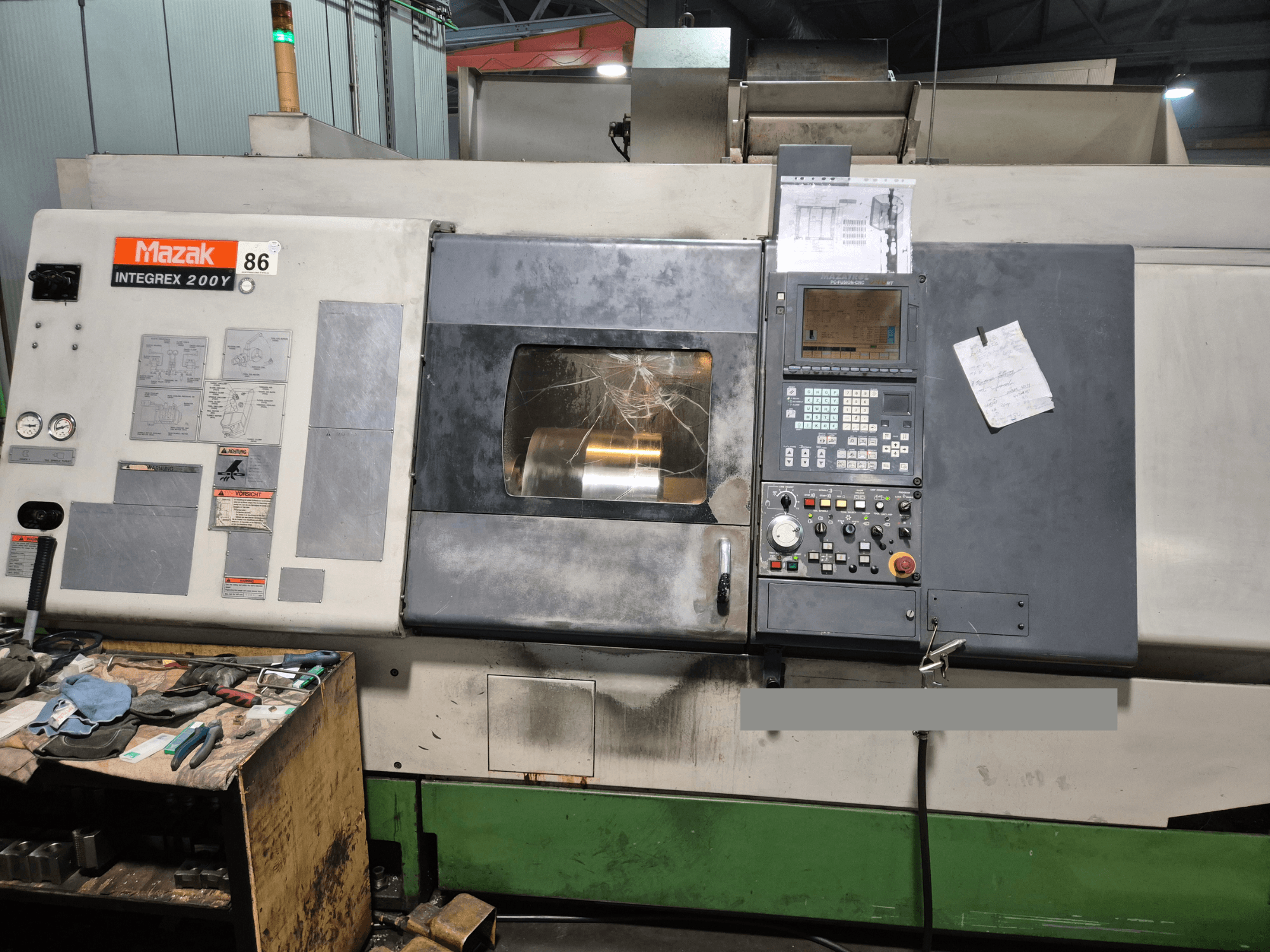 Mazak Integrex 200Y esztergagép, előlnézet, vezérlőpanel és szerszámok egy padon. Láthatóak a műszerek és a kijelző képernyő.