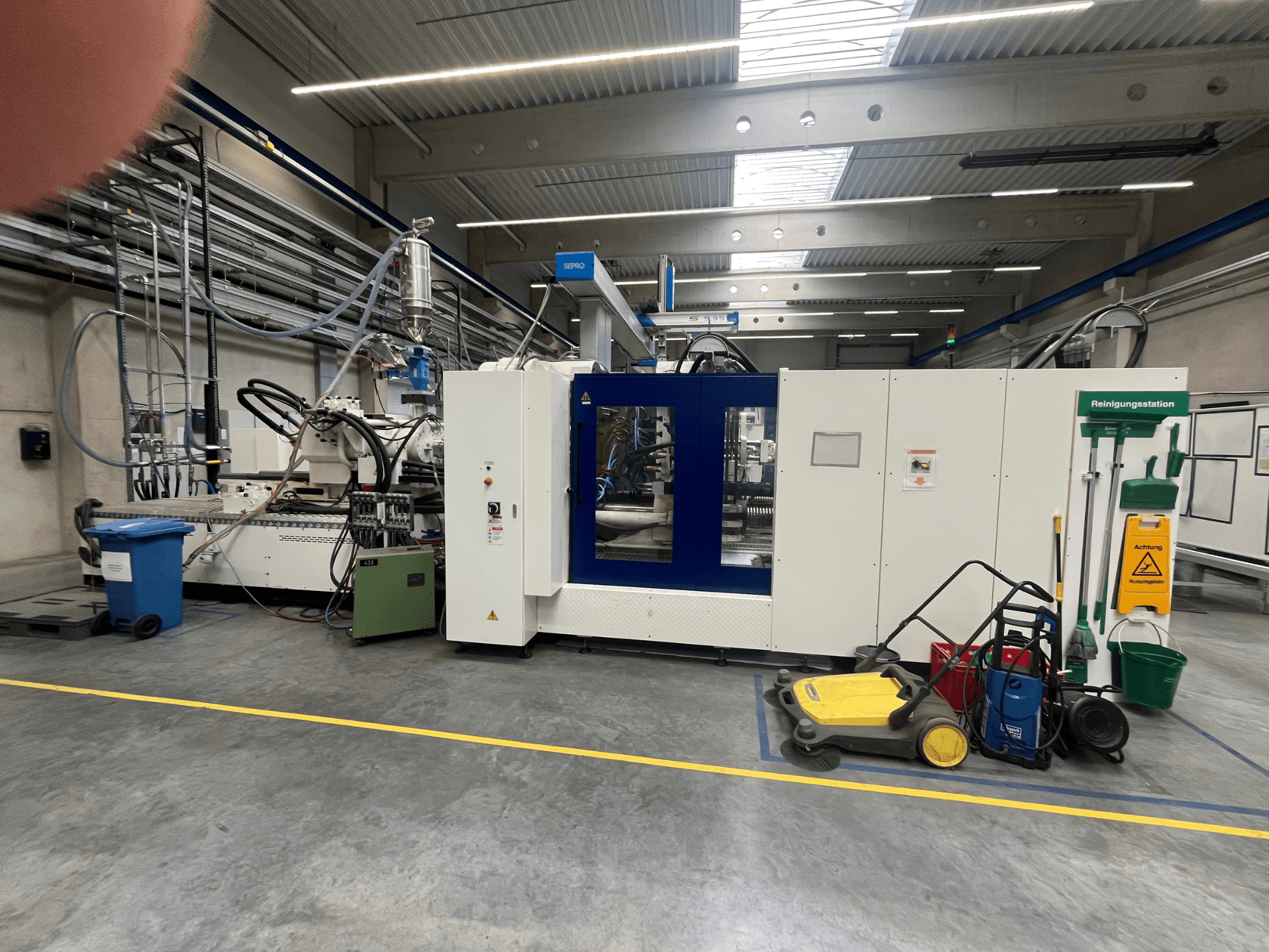 Ipari gép egy gyárban, elölnézetben, kék és fehér panelekkel, tömlőkkel és tisztítóberendezésekkel a közelben.