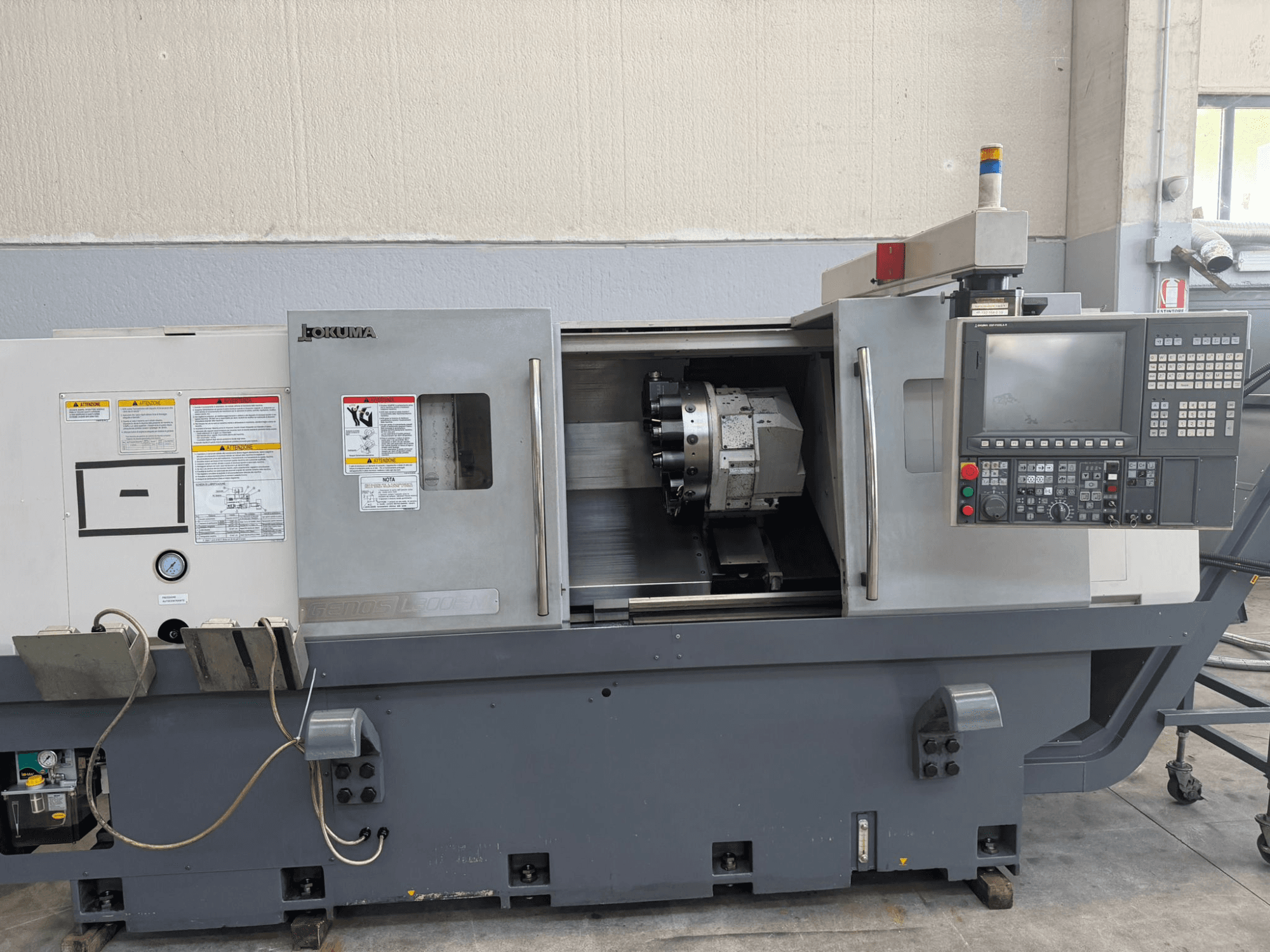 Okuma CNC esztergagép, előlnézet, a vezérlőpanel, a vágószerszámtartó és az oldalsó biztonsági figyelmeztetések.