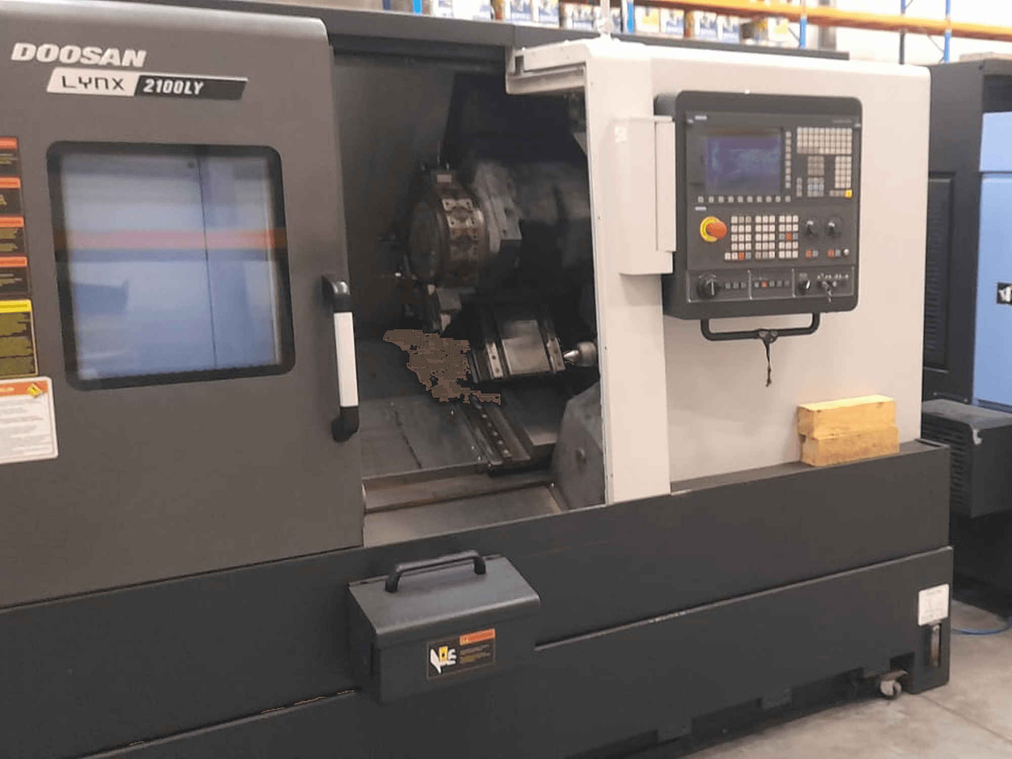 Doosan Lynx 2100LY CNC eszterga, elölnézetben a vezérlőpanel, a szerszámtartó és a belső munkaterület; láthatóak a műszaki címkék.