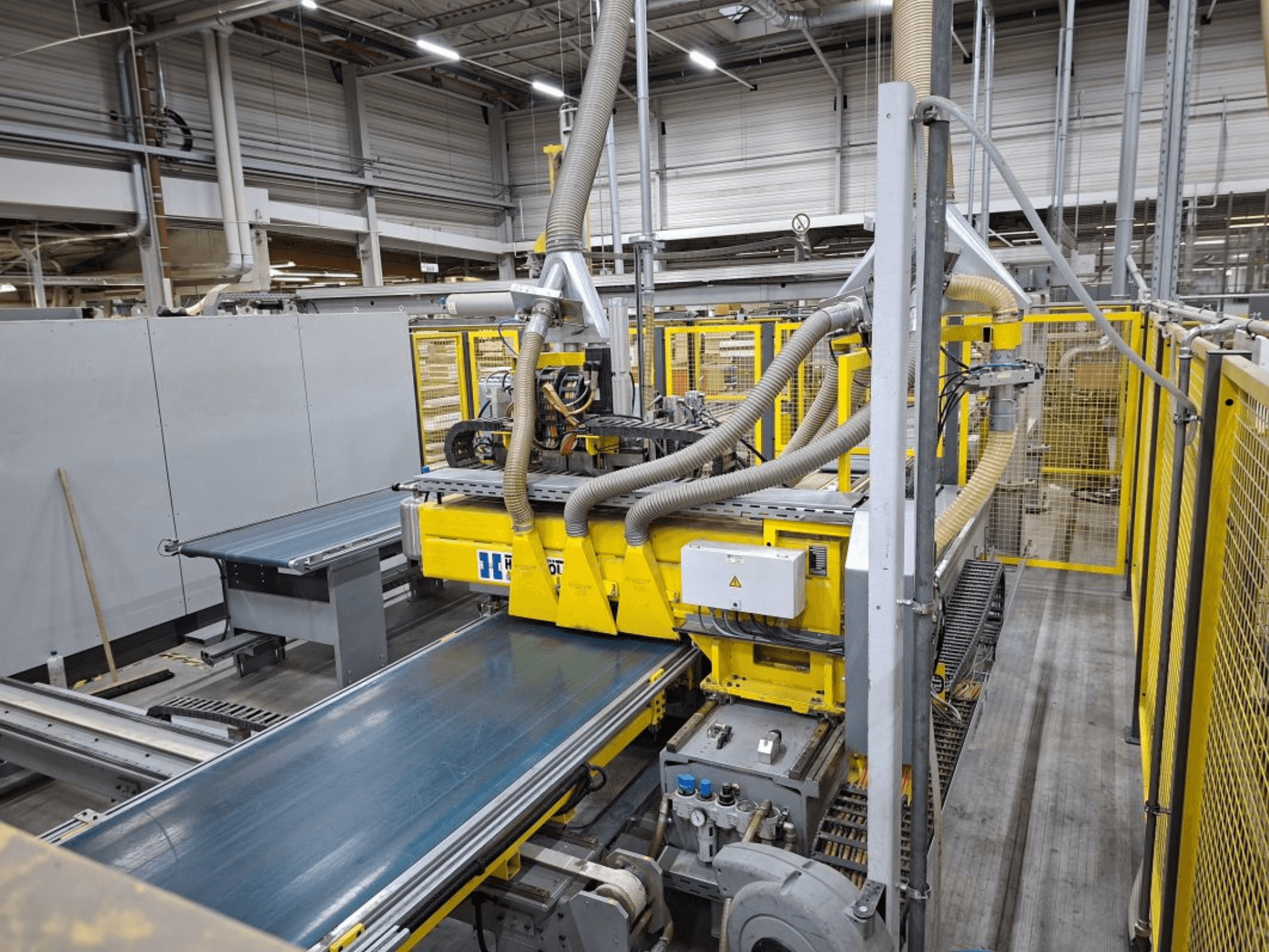 Ipari szállítószalagrendszer oldalnézetből, sárga gépekkel, vezérlőpanellel és a gyártáshoz szükséges tömlőcsatlakozásokkal.