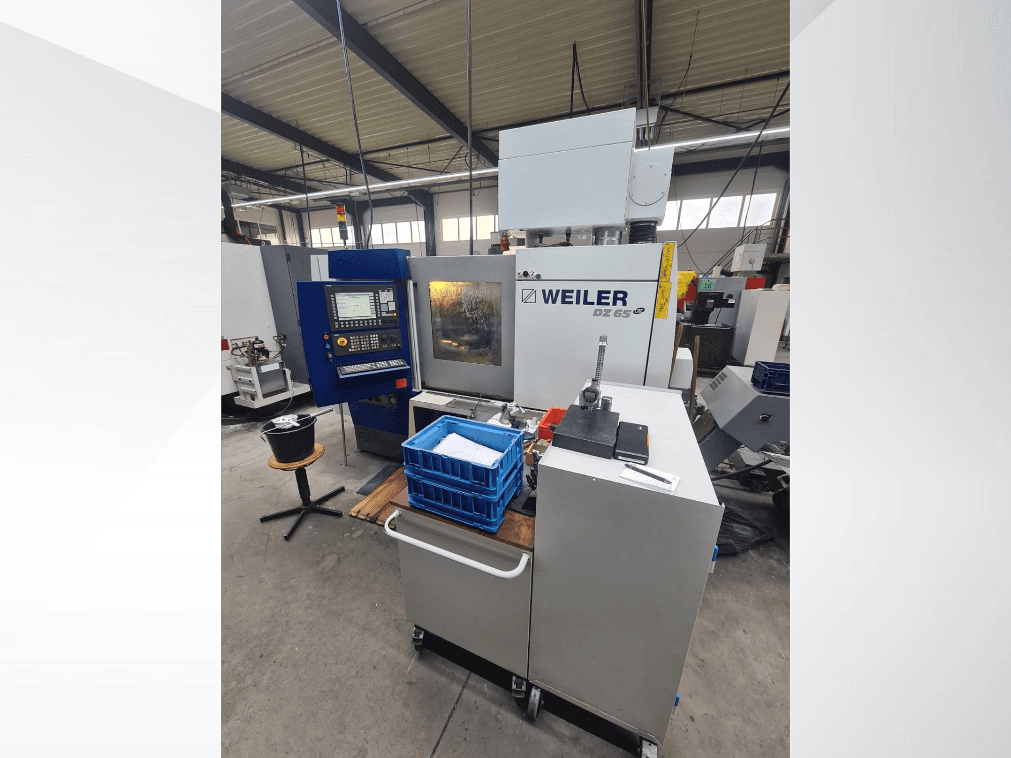 Weiler DZ 65 CNC-gép egy műhelyben, elölnézetben a vezérlőpanel, a szerszámok és a kék tárolórekeszek láthatóak.