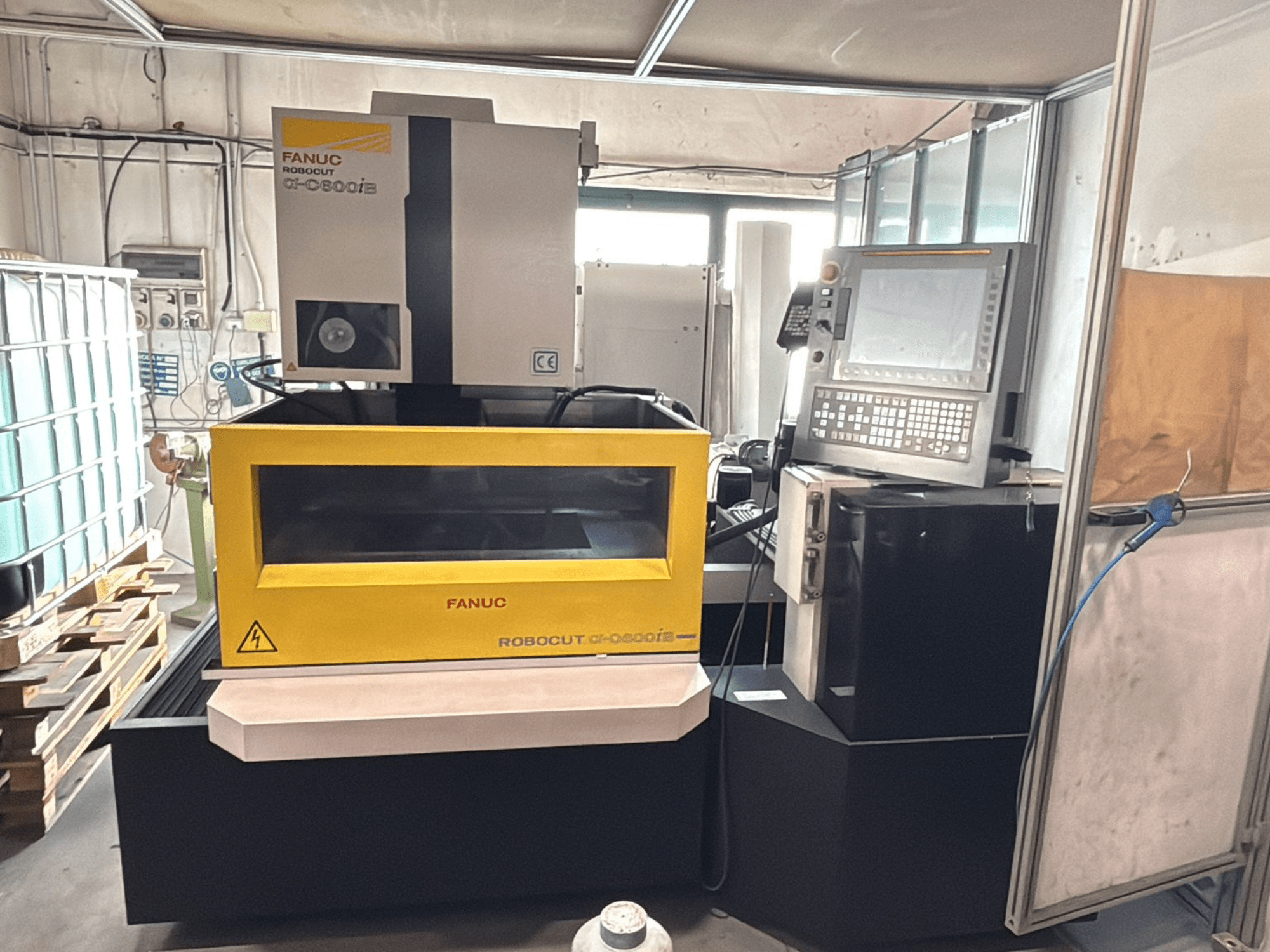 Egy FANUC Robocut α-0iE CNC-gép előlapja sárga burkolattal, a vezérlőpanel és a kijelző bemutatásával.