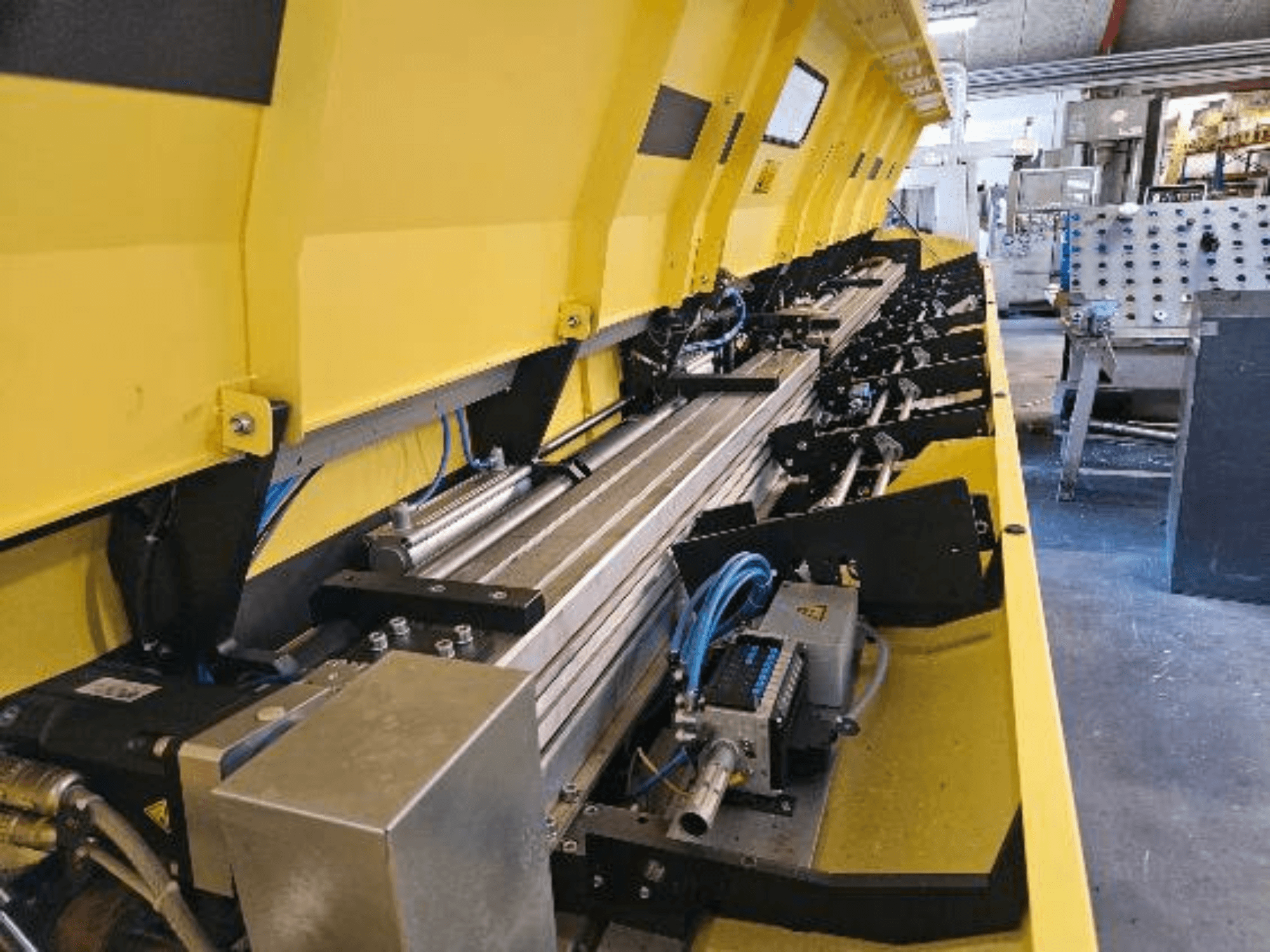 Közelkép egy sárga színű hidraulikus gépről, fém alkatrészekkel és szállítószalagokkal, tömlőkkel és elektronikus alkatrészekkel.