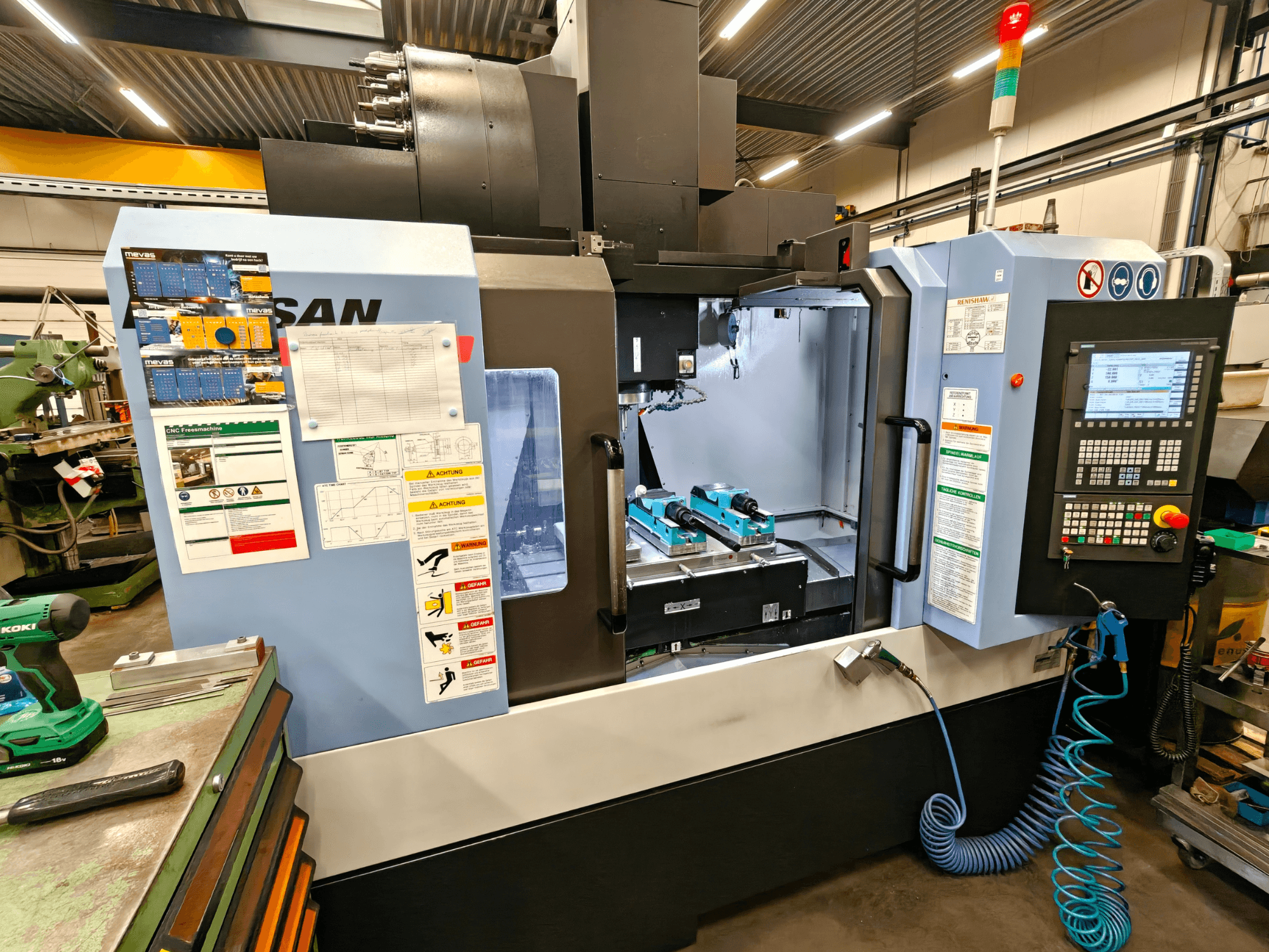 DOOSAN DNM 400 II függőleges megmunkálóközpont egy műhelyben, kezelőszervekkel, szerszámtartókkal és biztonsági jelzésekkel, elölnézetből.