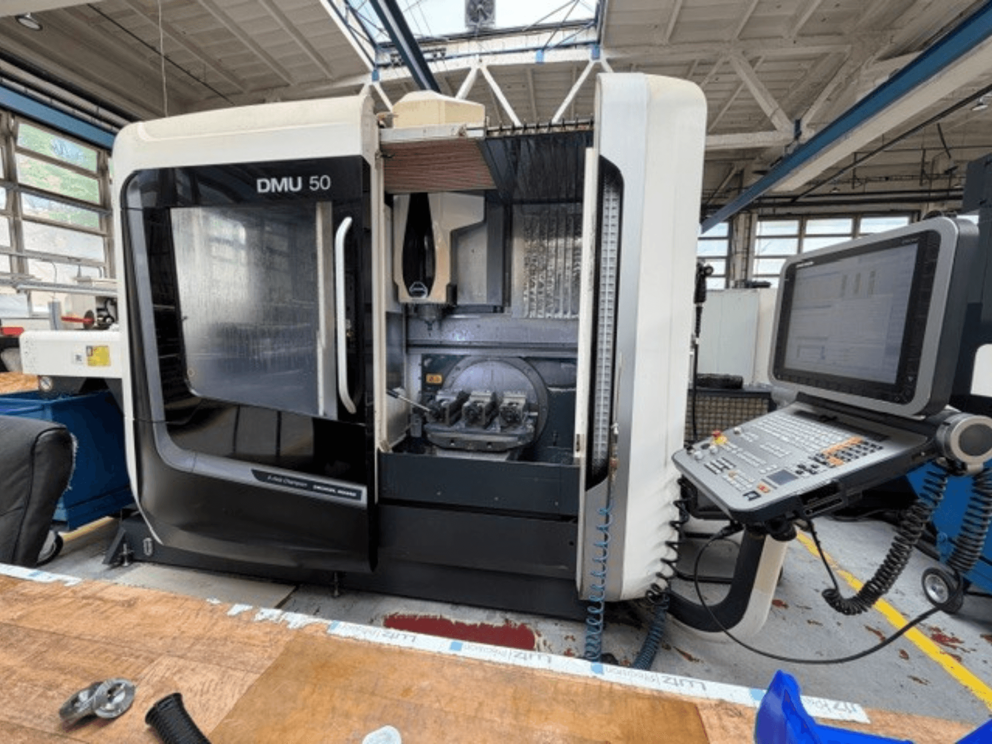 A DMG MORI DMU 50 harmadik generációs függőleges megmunkáló központ elölről látható, nyitott ajtóval, látható CNC-vezérlőpanellel és a belső munkaterülettel.