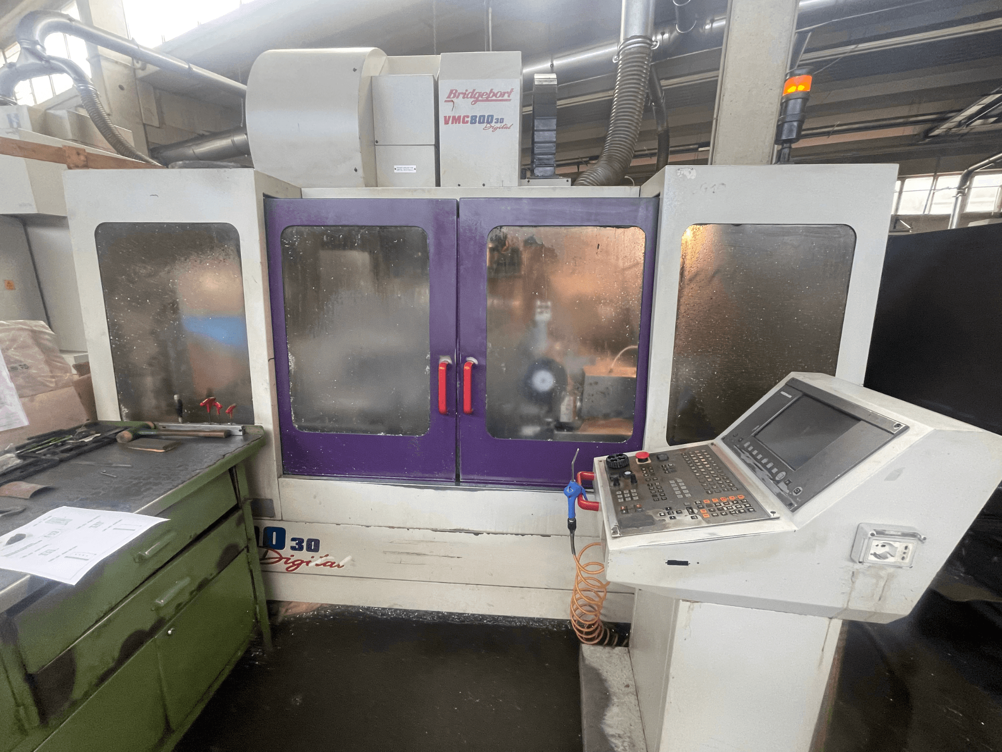 Bridgeport VMC 800/30 függőleges megmunkáló központ, elölnézet, a vezérlőpanellel és a lila ajtókkal, a szerszámok a szomszédos felületen.