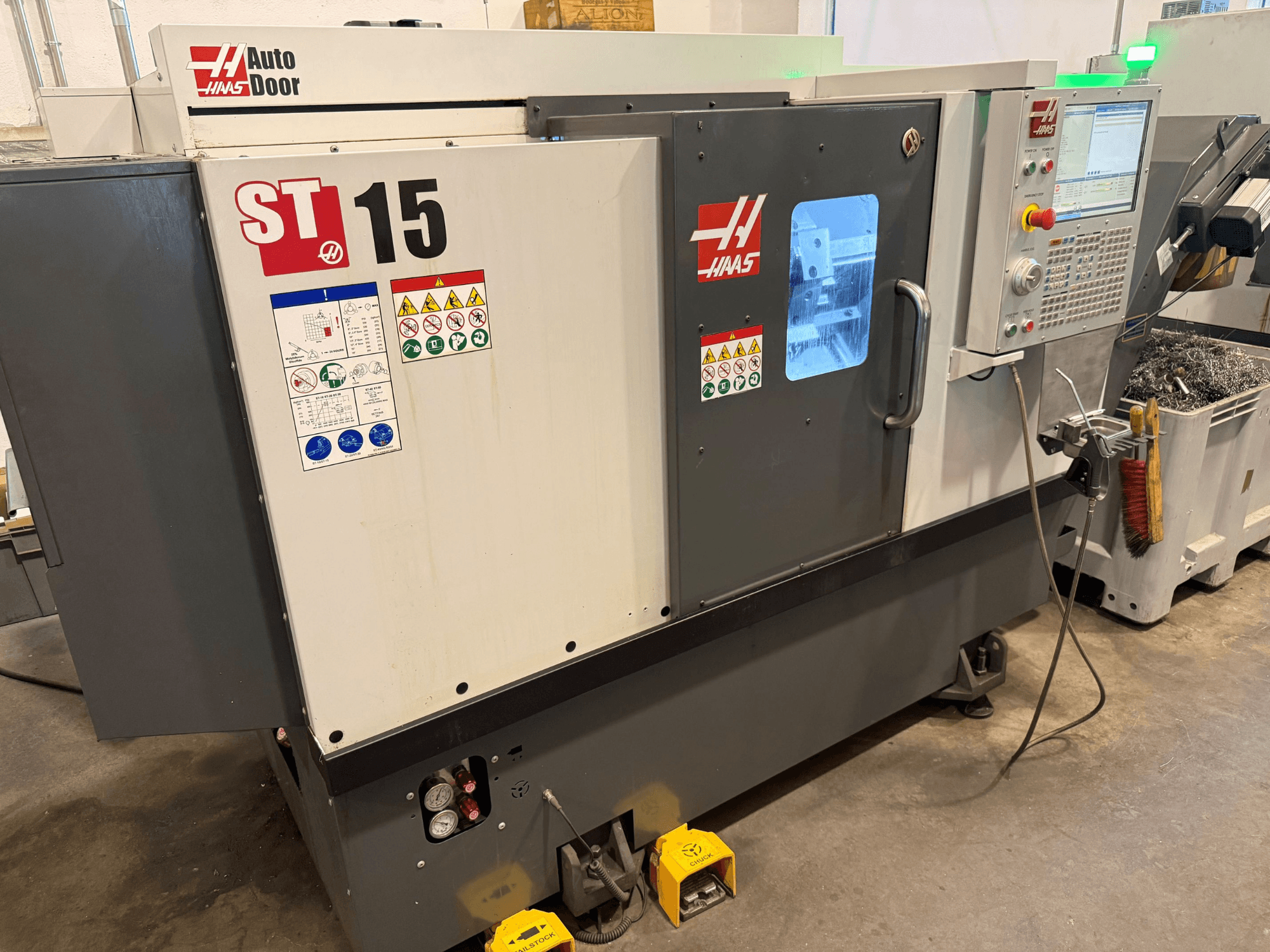 HAAS ST 15 vízszintes eszterga, elölnézet, amelyen látható a kezelőpanel, az automatikus ajtó és a műszaki kijelzők.