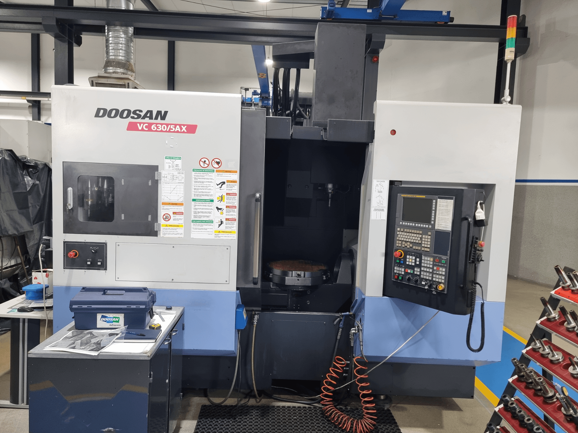 DOOSAN VC 630/5AX univerzális megmunkáló központ, elölnézet, amelyen látható a vezérlőpanel, a megmunkálási terület és a biztonsági felszerelések.