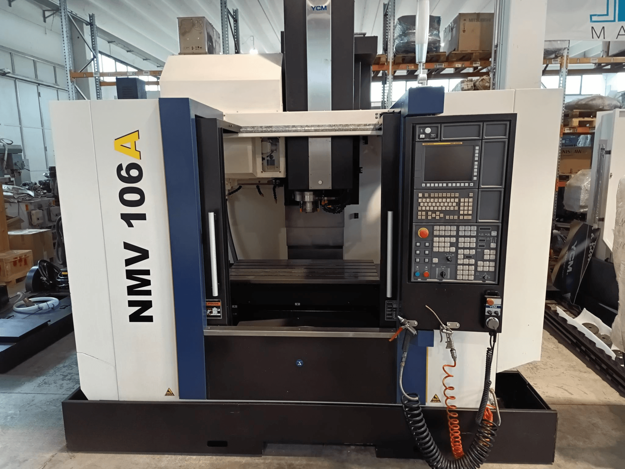 YCM NMV 106A megmunkálóközpont, elölnézet, a gombokkal és hűtőfolyadéktömlőkkel ellátott vezérlőpanel.