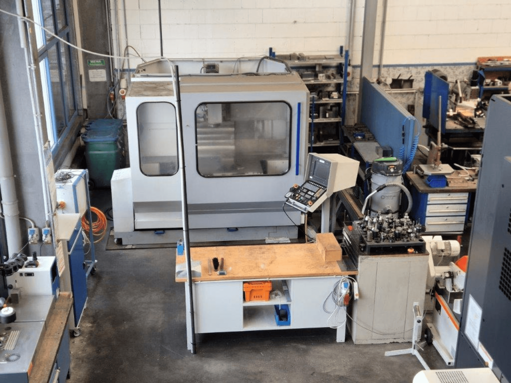 CNC marógép egy műhelyben, elölnézetben, a háttérben a vezérlőpanel, a munkafelület és a szerszámok láthatóak.