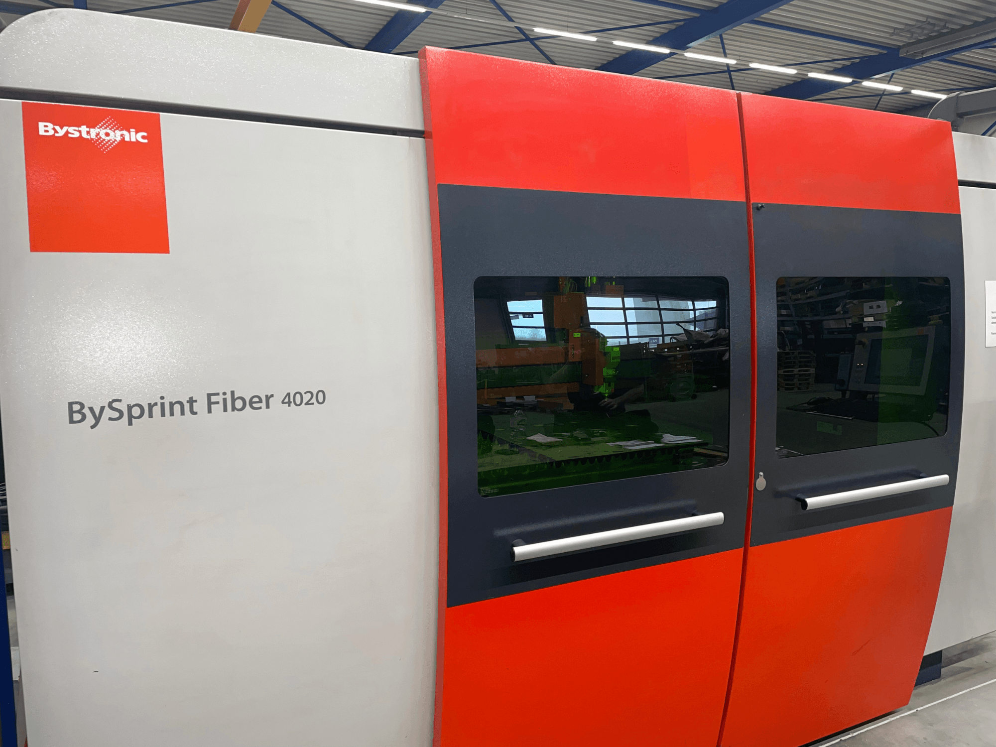 Bystronic BySprint Fiber 4020 elölnézetben, szürke és piros panel kialakítással, nagy ablakokkal és belülről látható kezelőfelülettel.