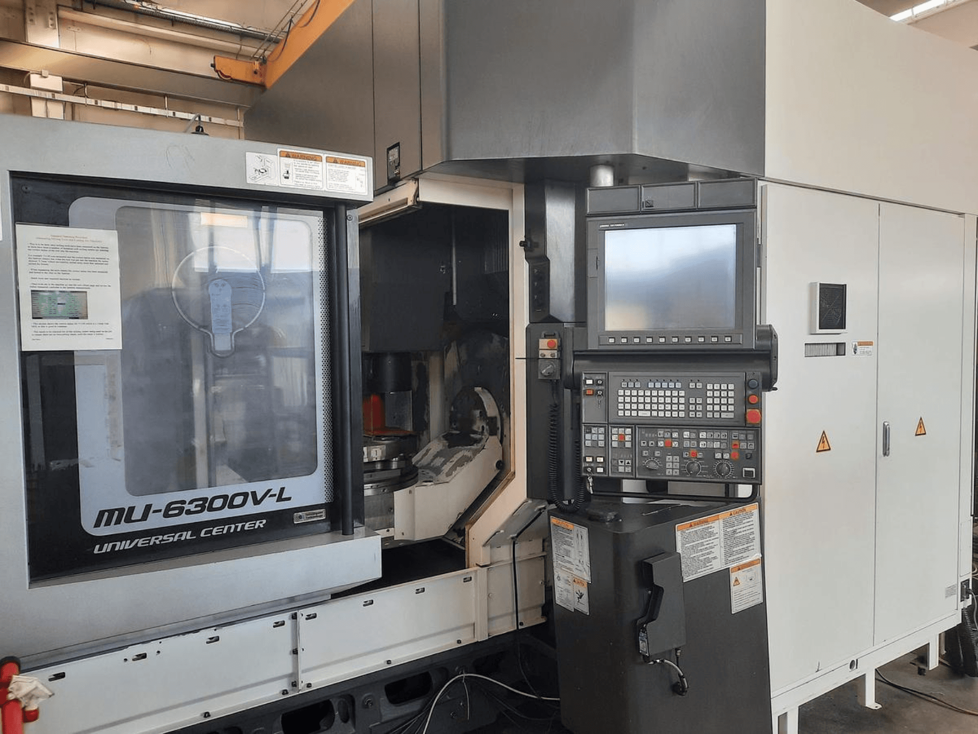 MU-6300V-L Universal Center gép szemből, a vezérlőpanel, a képernyő és a kezelési útmutató látható.