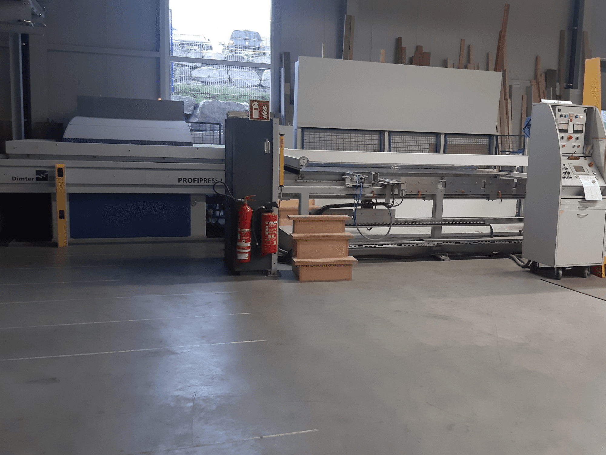 Dimter ProfiPress gép egy műhelyben, szemből nézve, a vezérlőpanel és a tűzoltó készülékek a közelben.