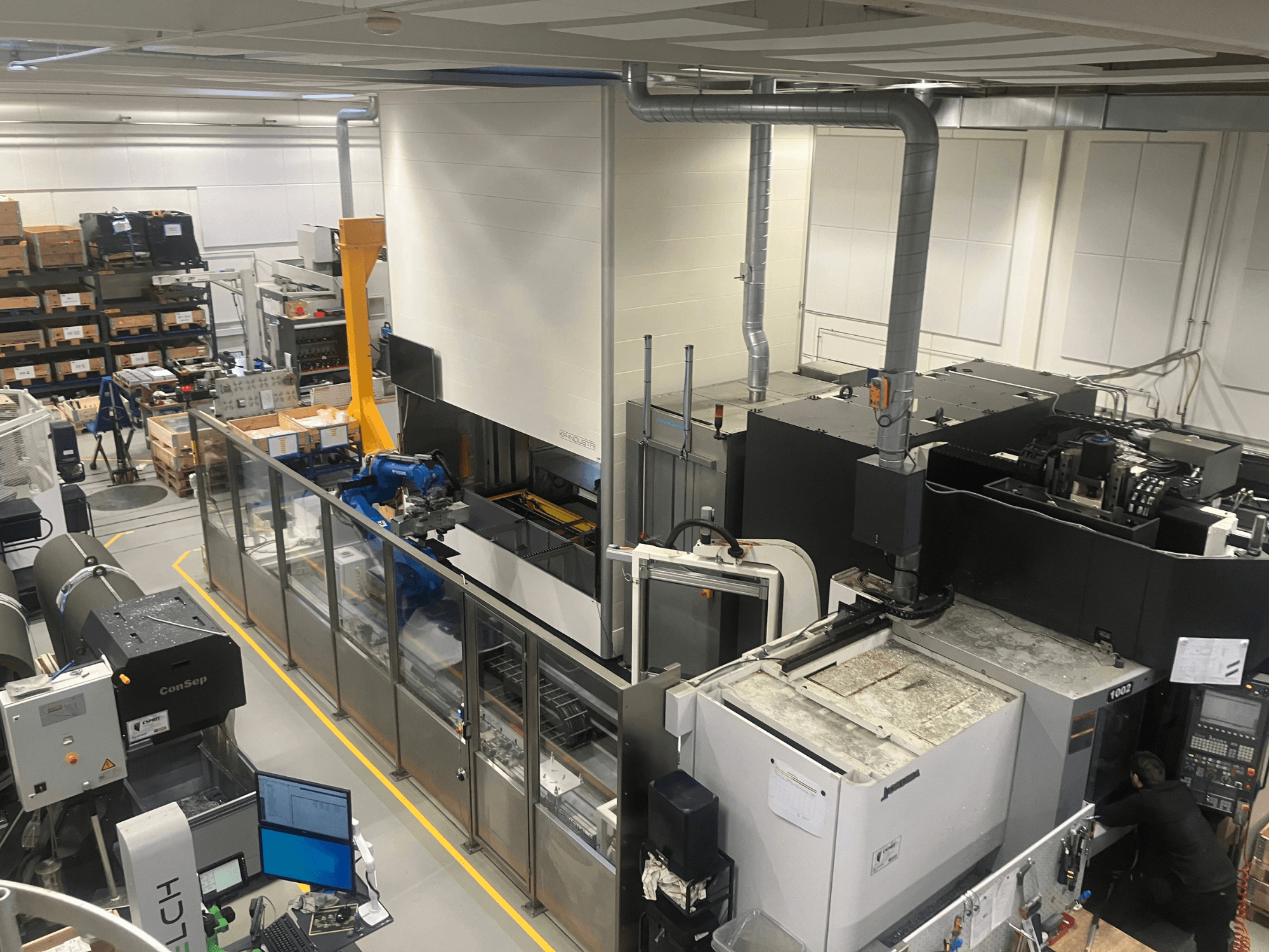 SSI SCHAFER Logimat automatizálási rendszer egy raktárban, elölnézet; robotkar, raktári állványok és gépek.