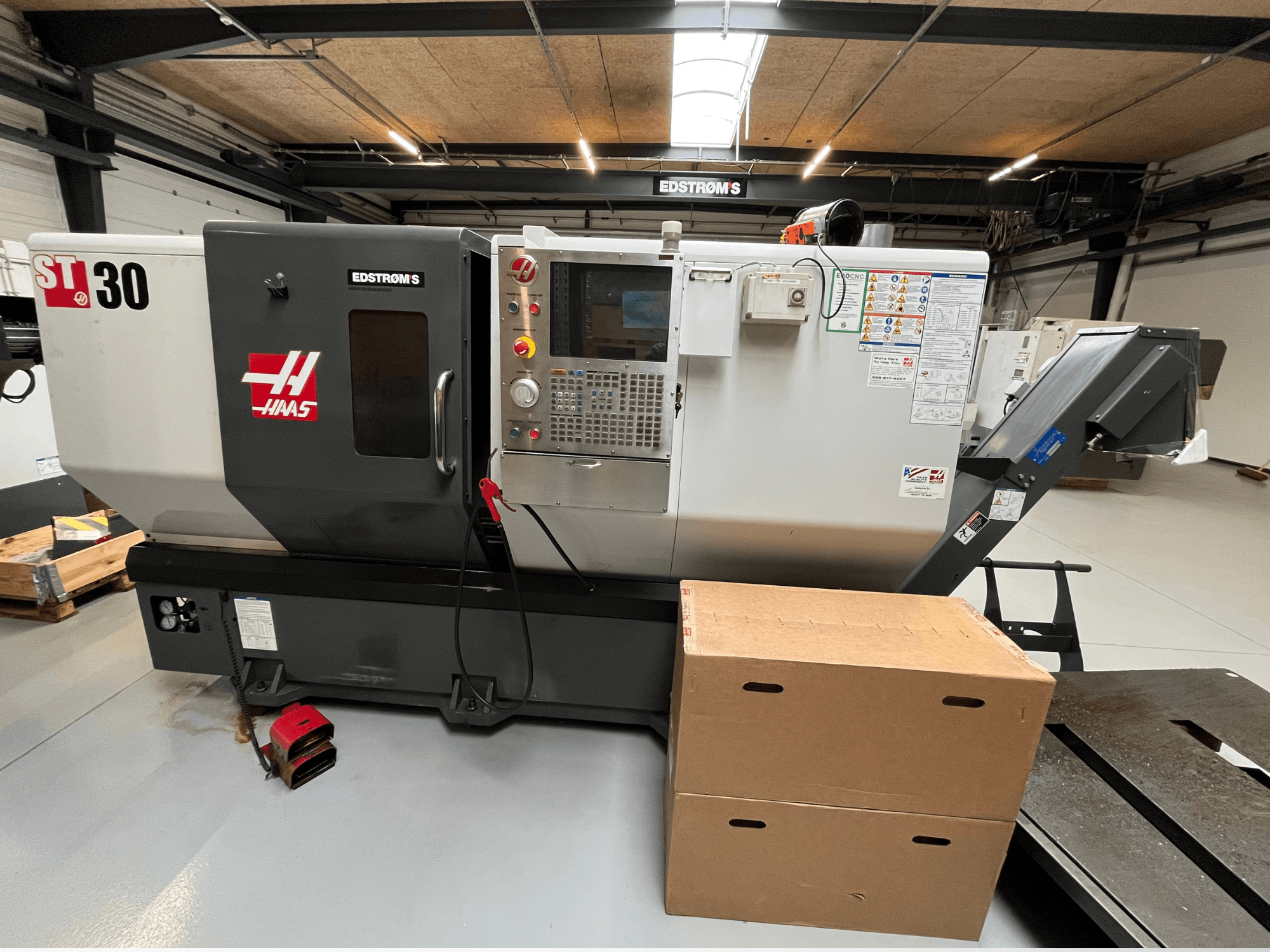 Haas ST-30 CNC eszterga oldalnézetből, a vezérlőpanel, a modelljelvény és két kartondoboz a közelben.